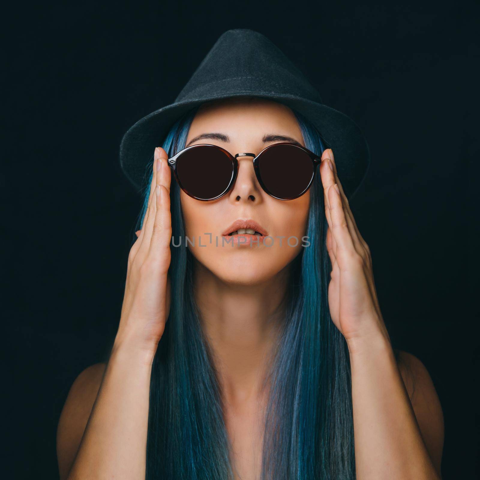 Beautiful young woman with long blue hair in round sunglasses and hat. Fashion and beauty
