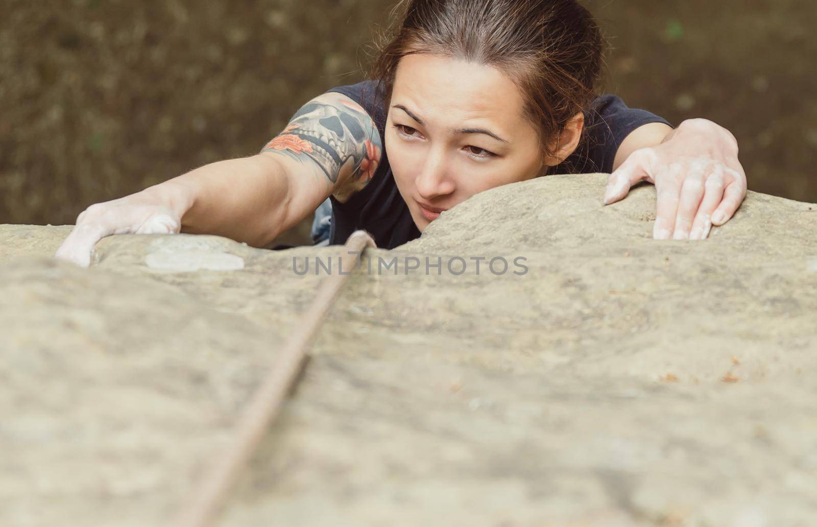 Sporty young woman wearing in safety equipment with rope climbing on peack of rock in summer outdoor, top view