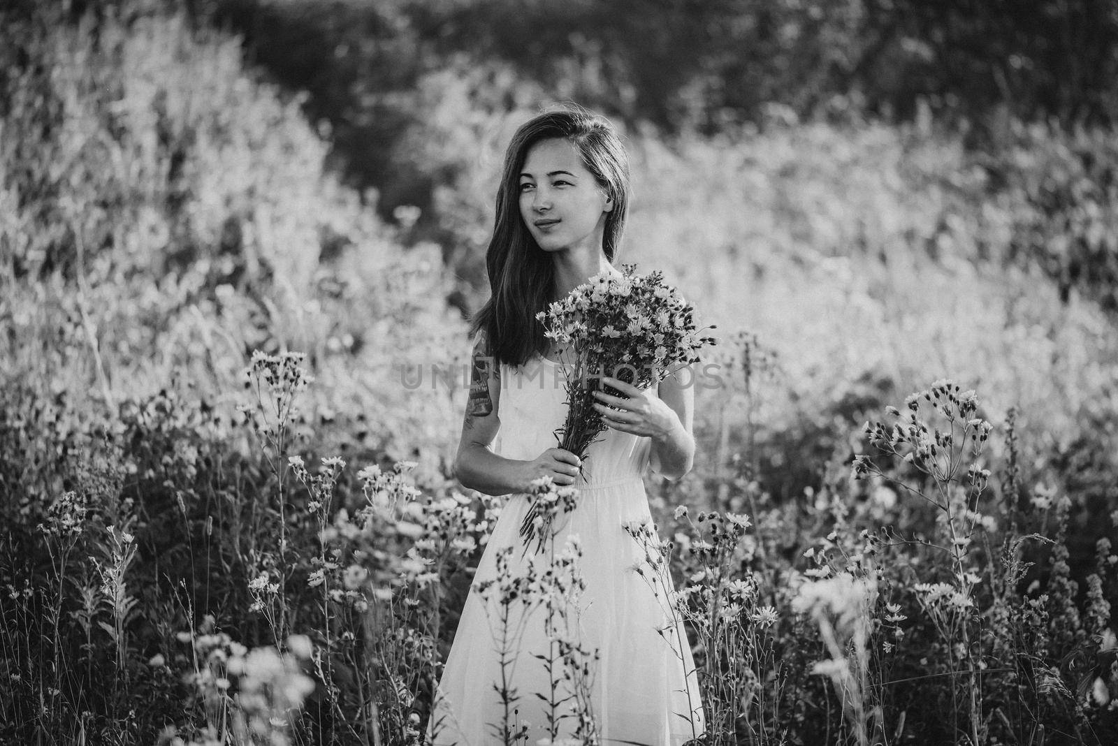 Beautiful young woman with blue hair and bouquet walking on flower field in summer. Black and white image. Effect film grain