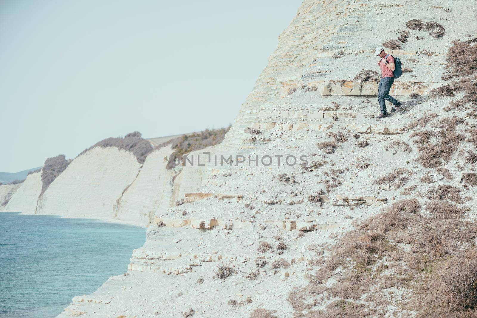 Hiker young man with backpack go down on stone mountain near the sea outdoor