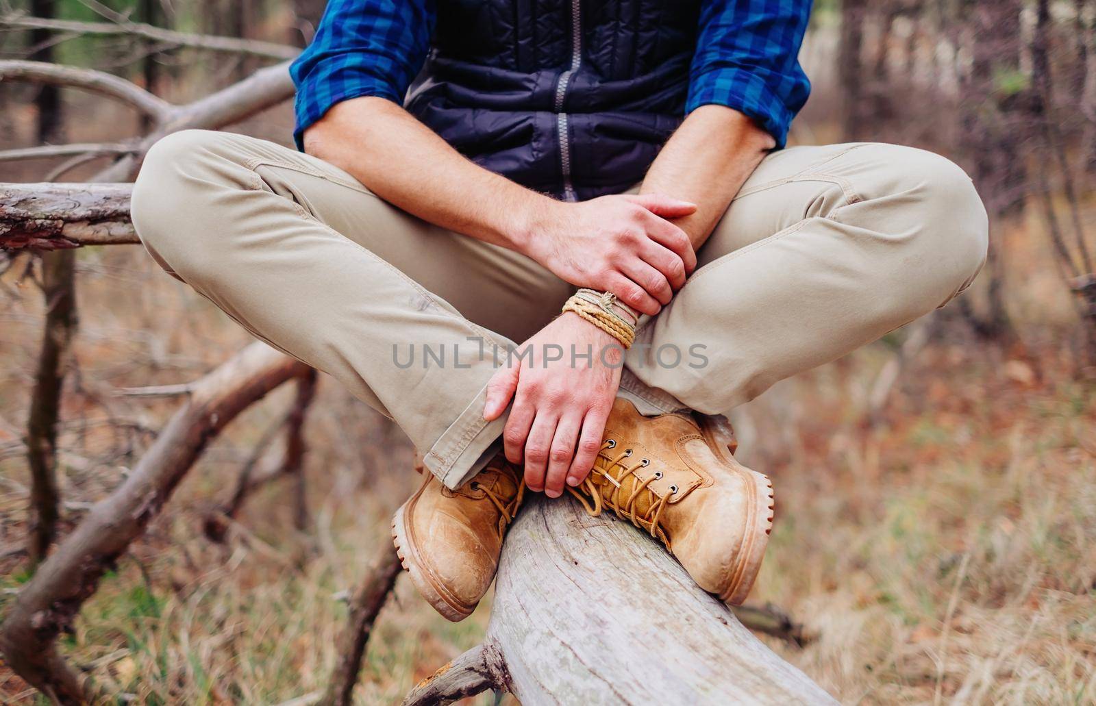 Unrecognizable traveler young man sitting on tree trunk, view of legs