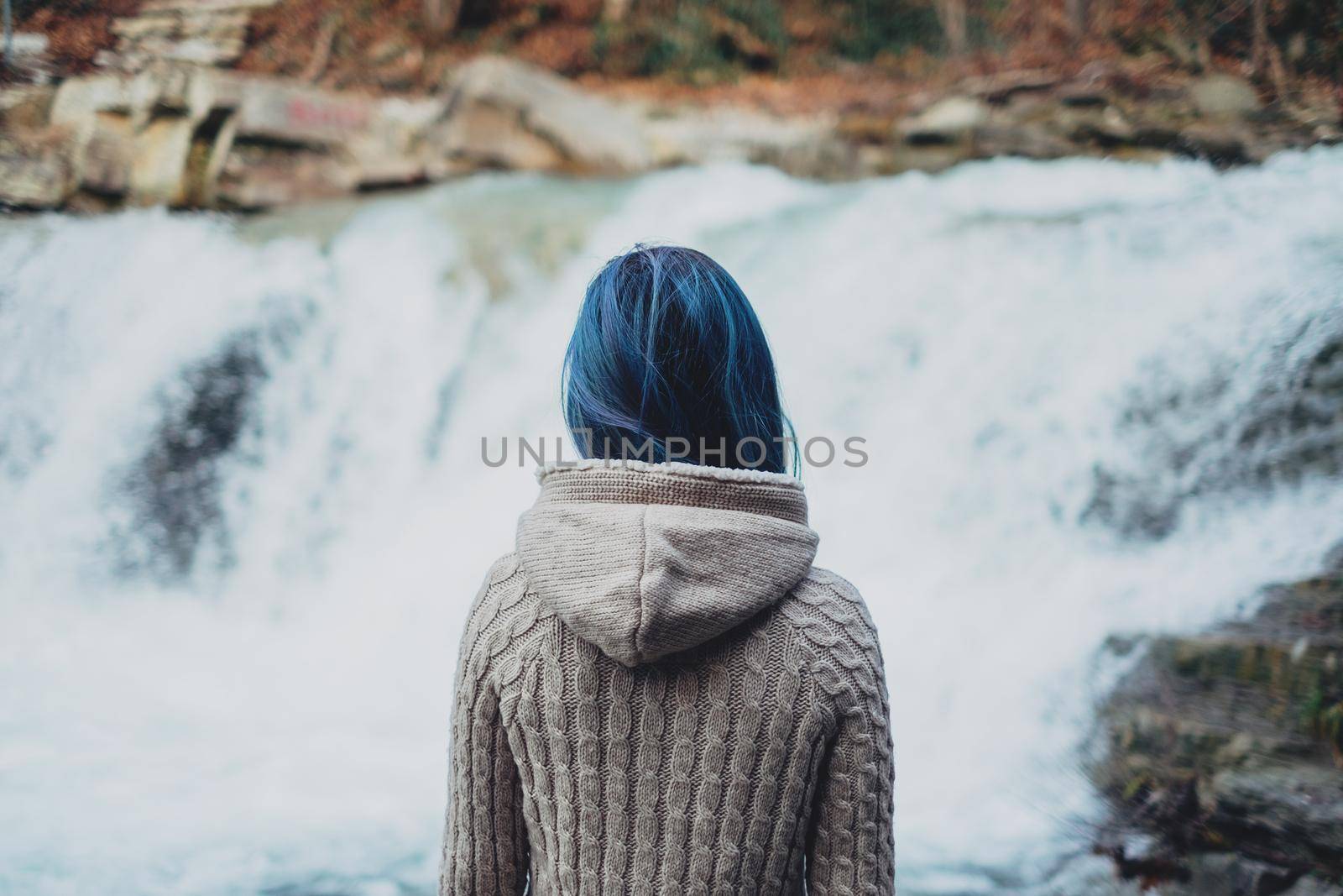 Traveler woman with blue hair looking at beautiful waterfall, rear view