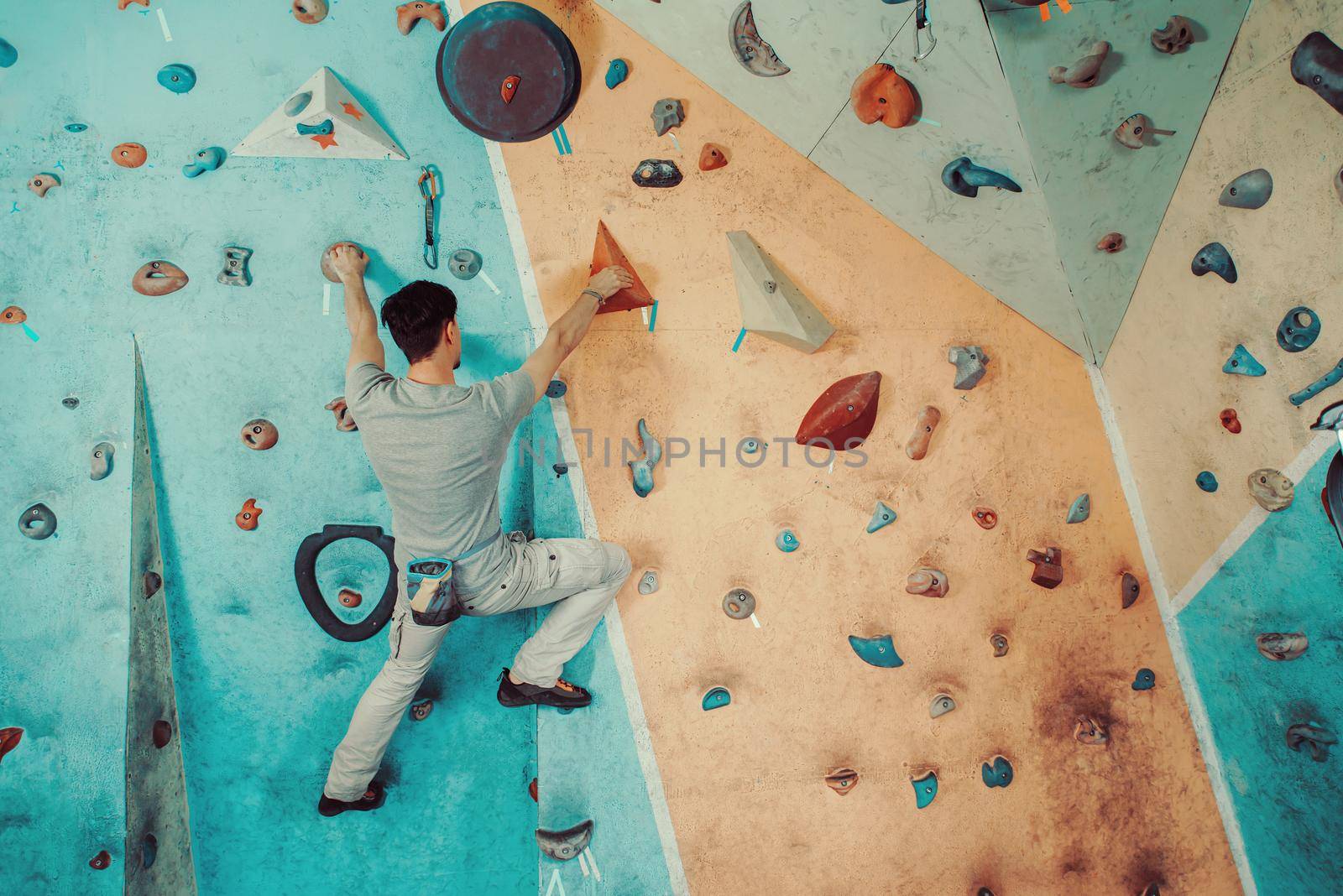 Young man climbing on artificial boulders wall indoor, rear view