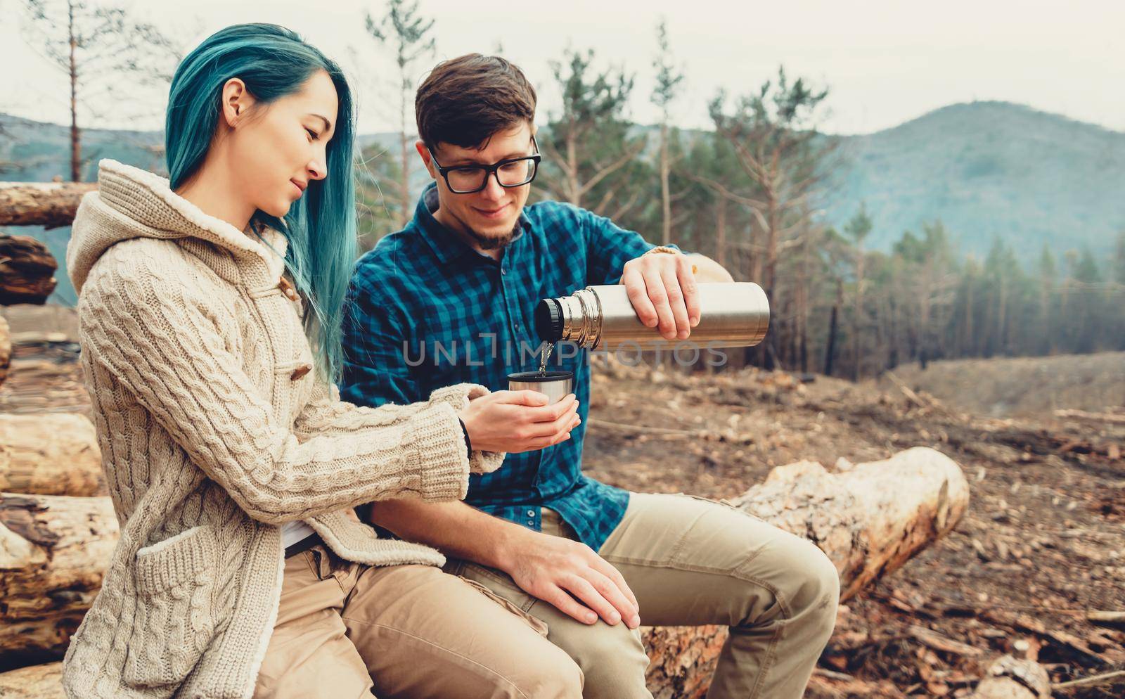 Loving couple resting outdoor. Young man pouring tea from thermos to cup of young woman in the forest