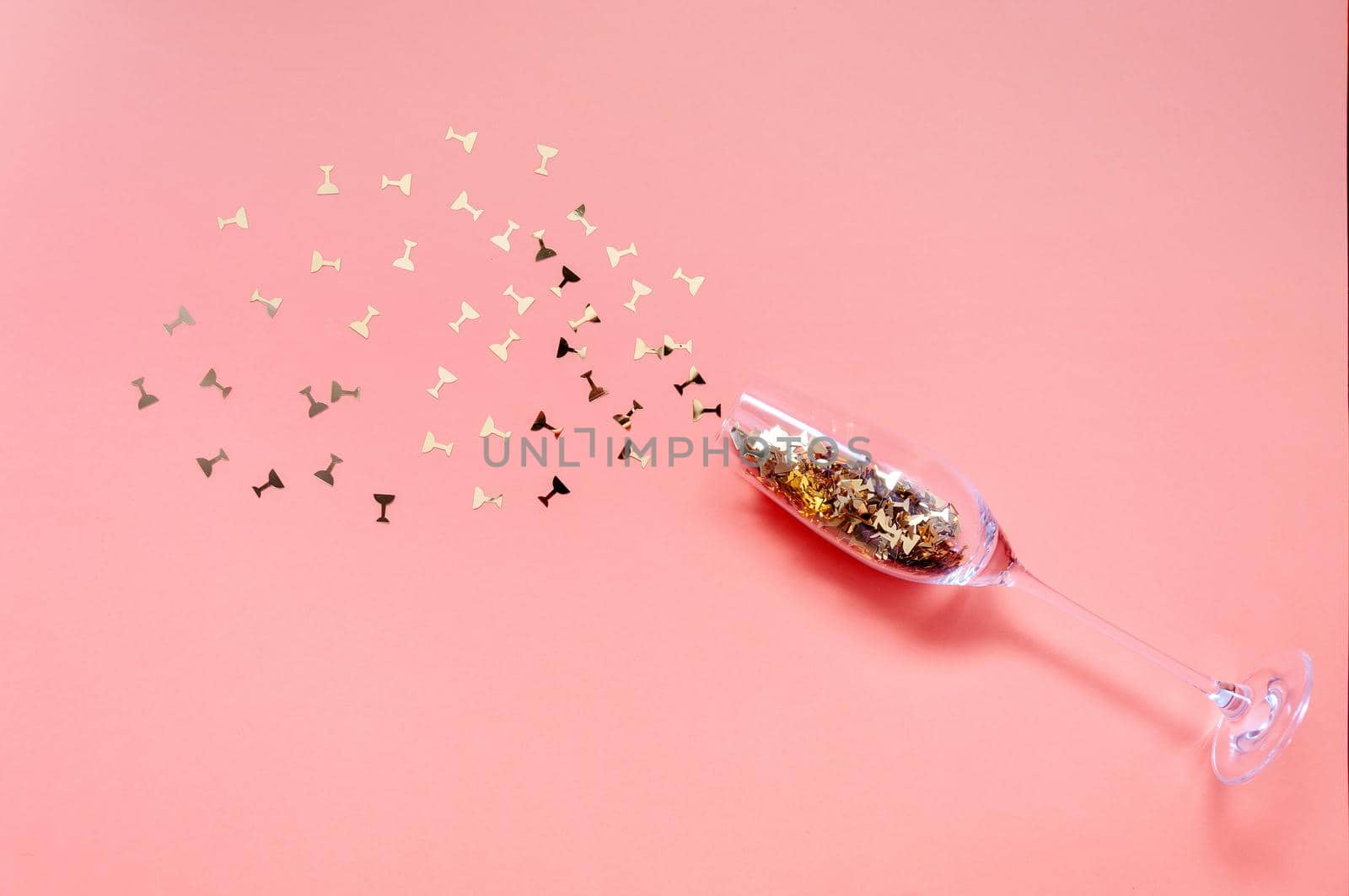 Champagne Glass with Golden Confetti on Pink Background. Creative Christmas Concept.