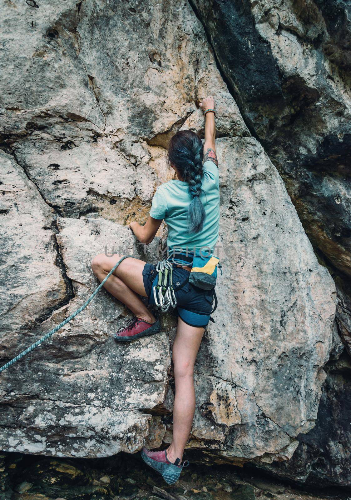 Unrecognizable young woman wearing in safety harness with equipment climbing the rock wall outdoor, rear view