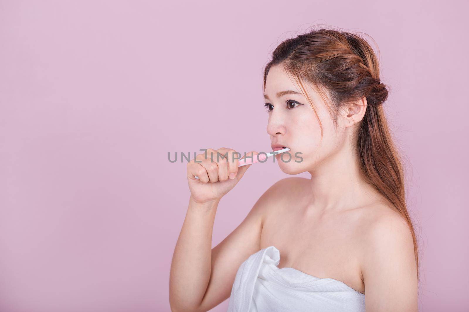 beautiful woman brushing her teeth on pink background