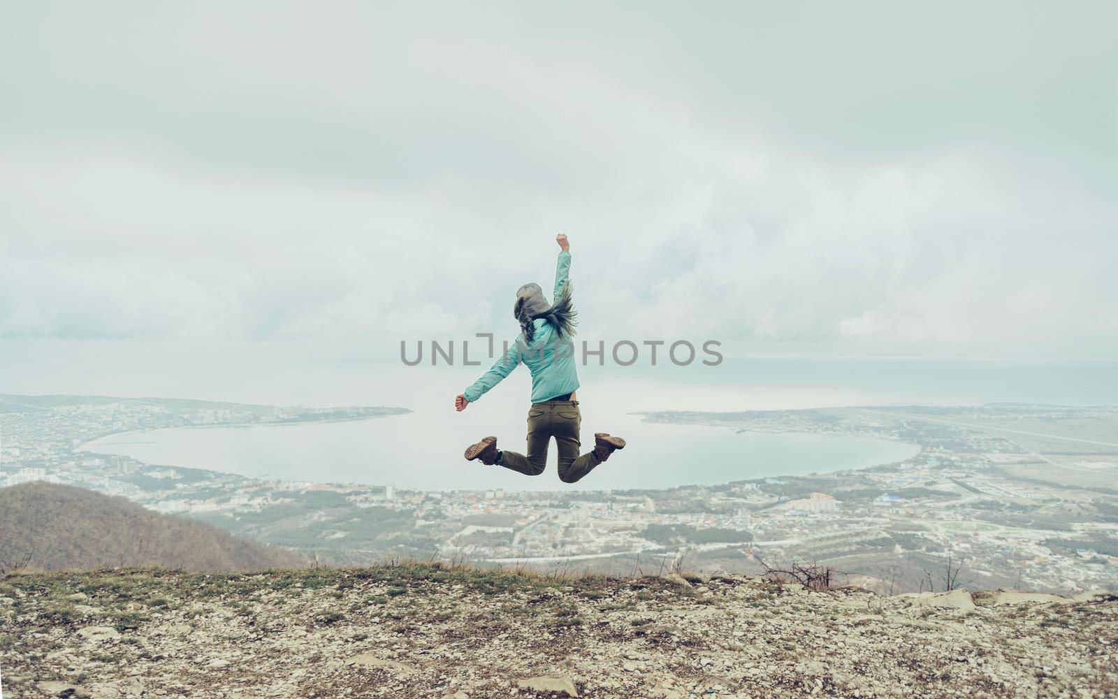 Happy traveler young woman jumping on mountain on background of sea bay, rear view