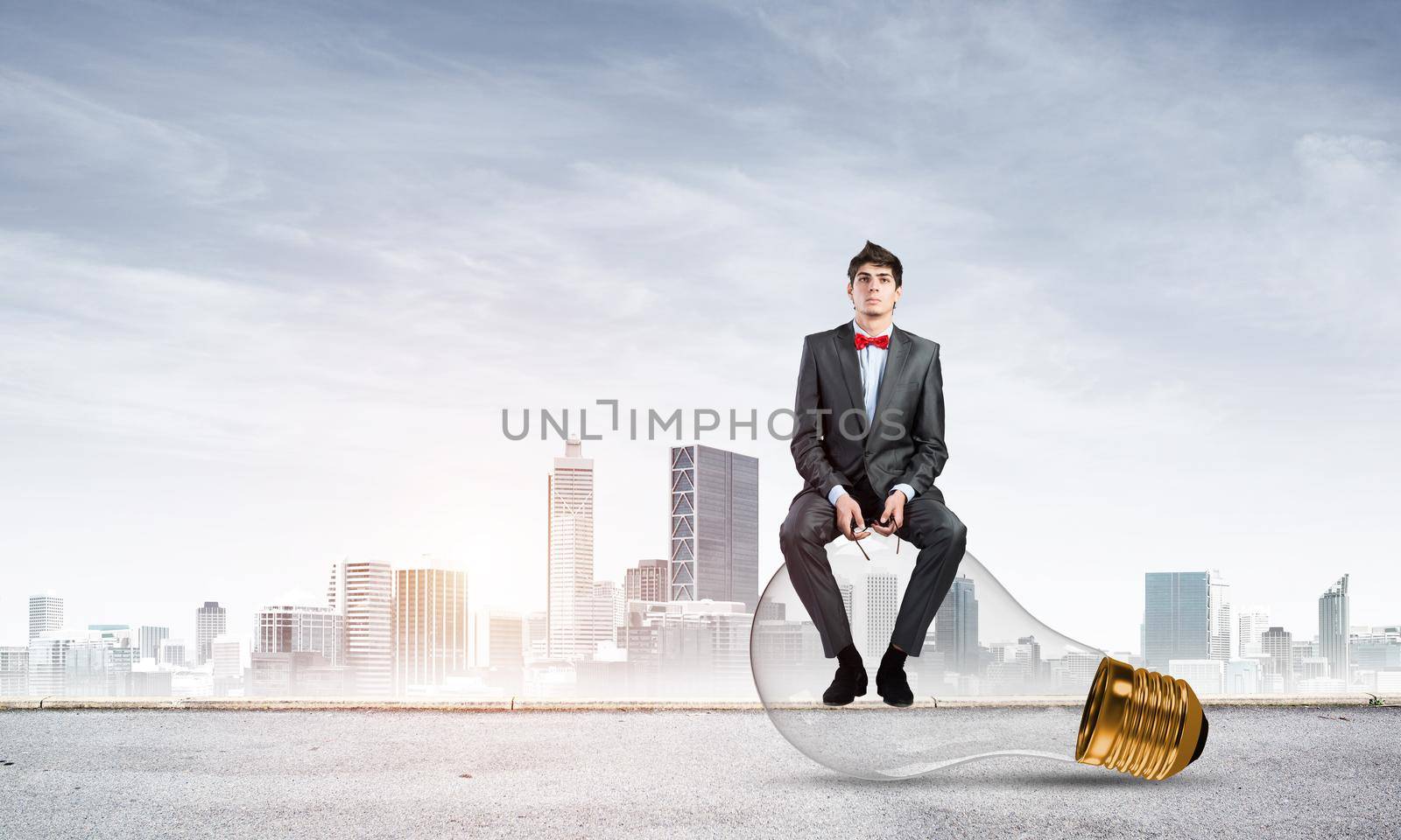 A businessman with glasses sits on a light bulb. concept of creativity in business