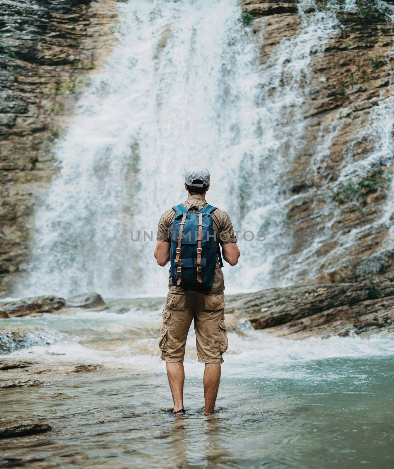 Explorer man looking at waterfall by alexAleksei