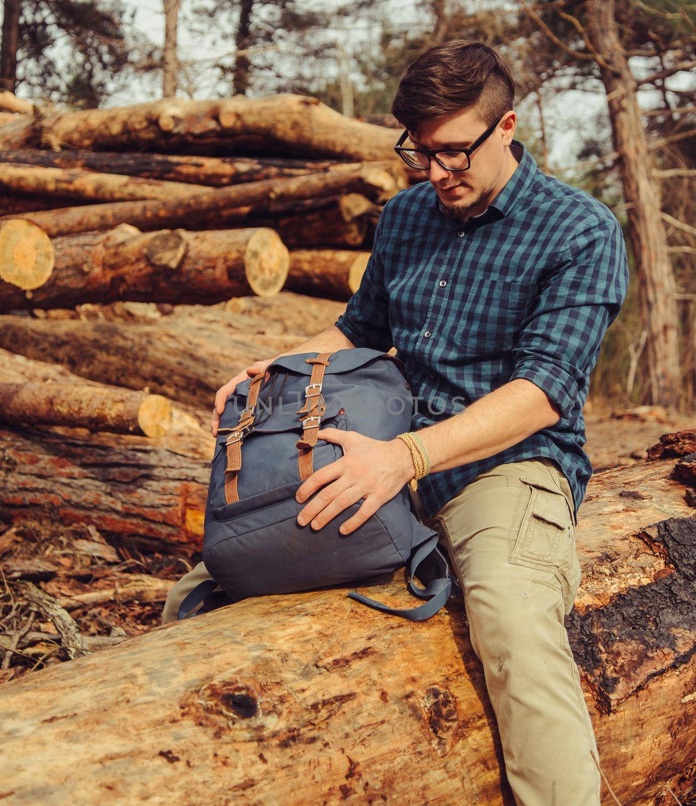 Hiker young man with backpack sitting on felled wood trunk outdoor