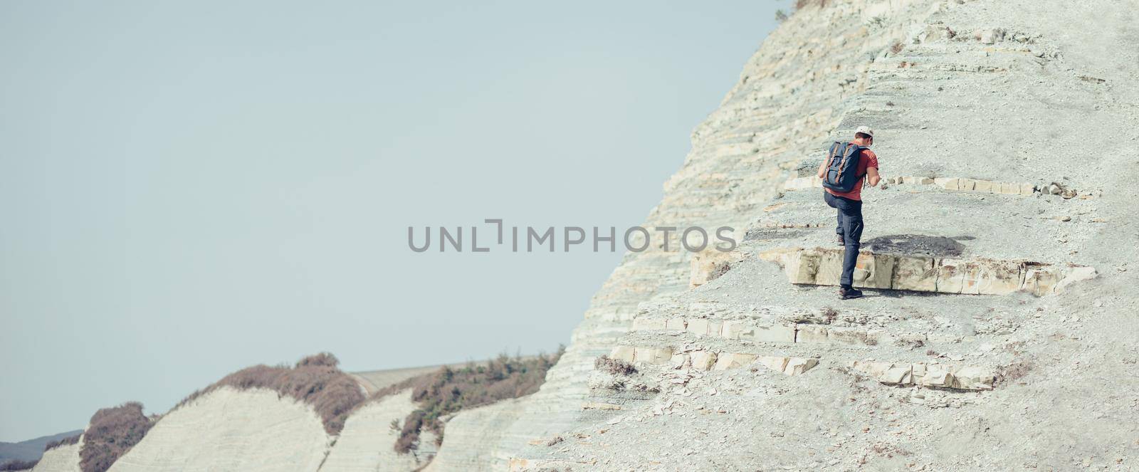 Hiker young man with backpack climbing on stone mountain outdoor