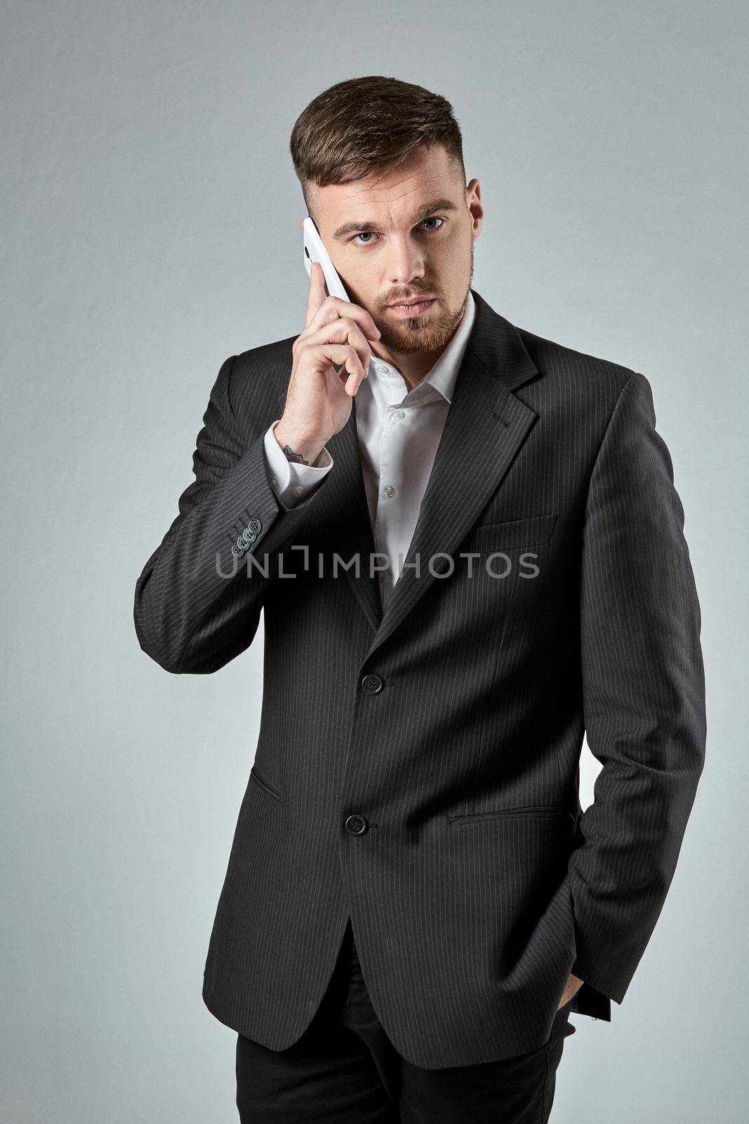 Portrait of a handsome businessman making a phone call against a grey background. Emotions. A man looks into the camera