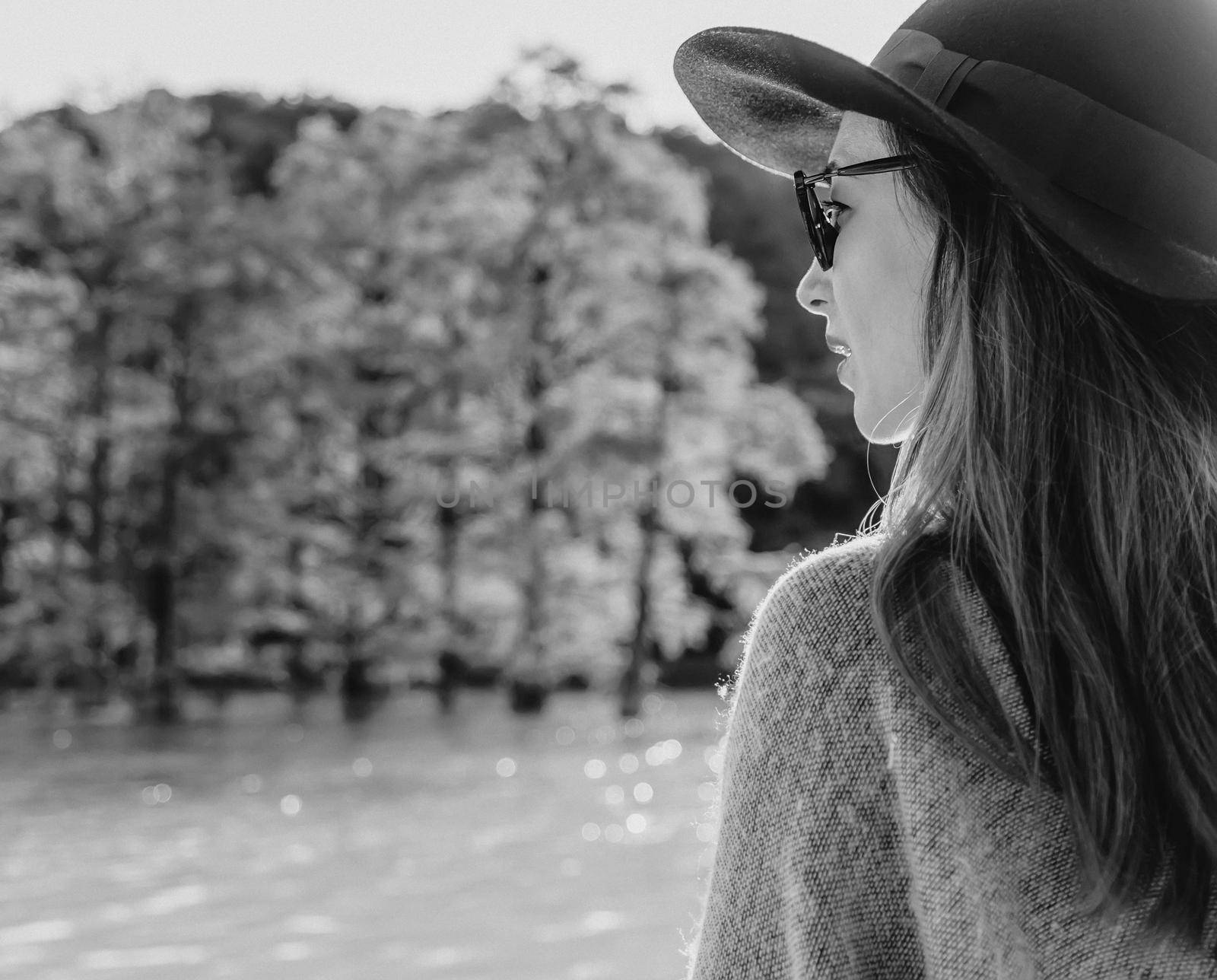 Beautiful young woman wearing in hat and sunglasses resting on lake in summer. Monochrome image