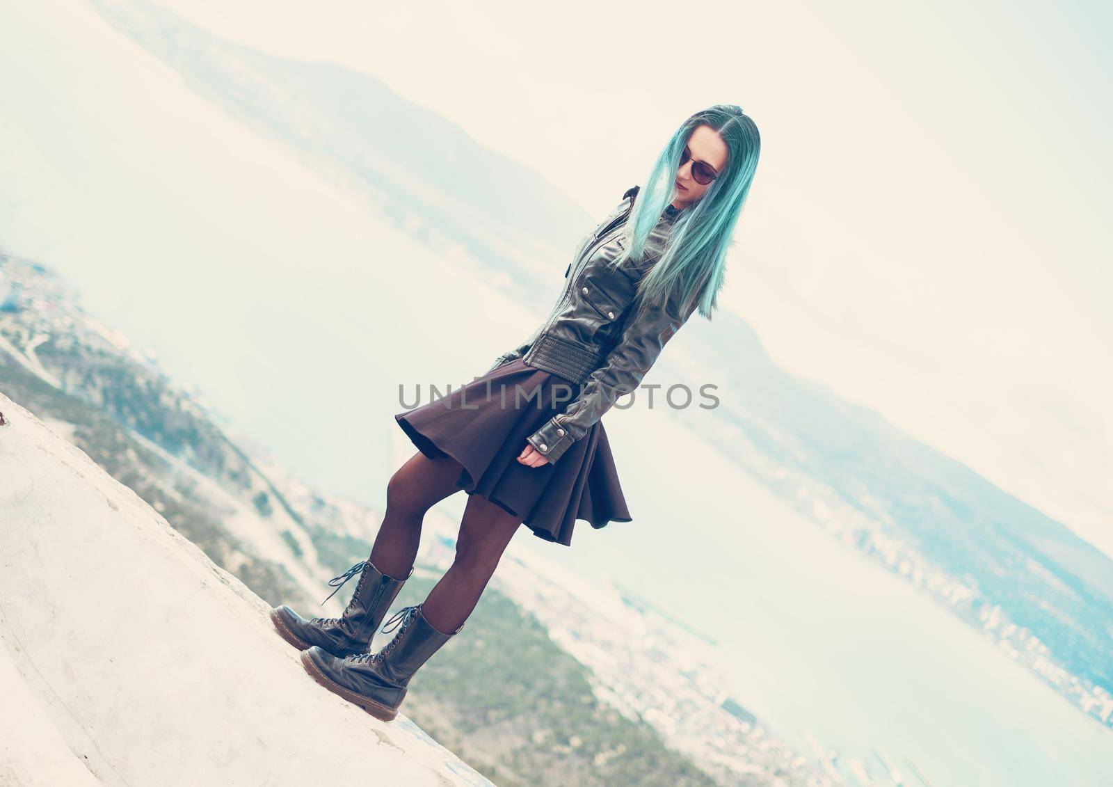 Dark style beautiful young woman wearing in black leather jacket and dress standing on edge over the sea bay outdoor