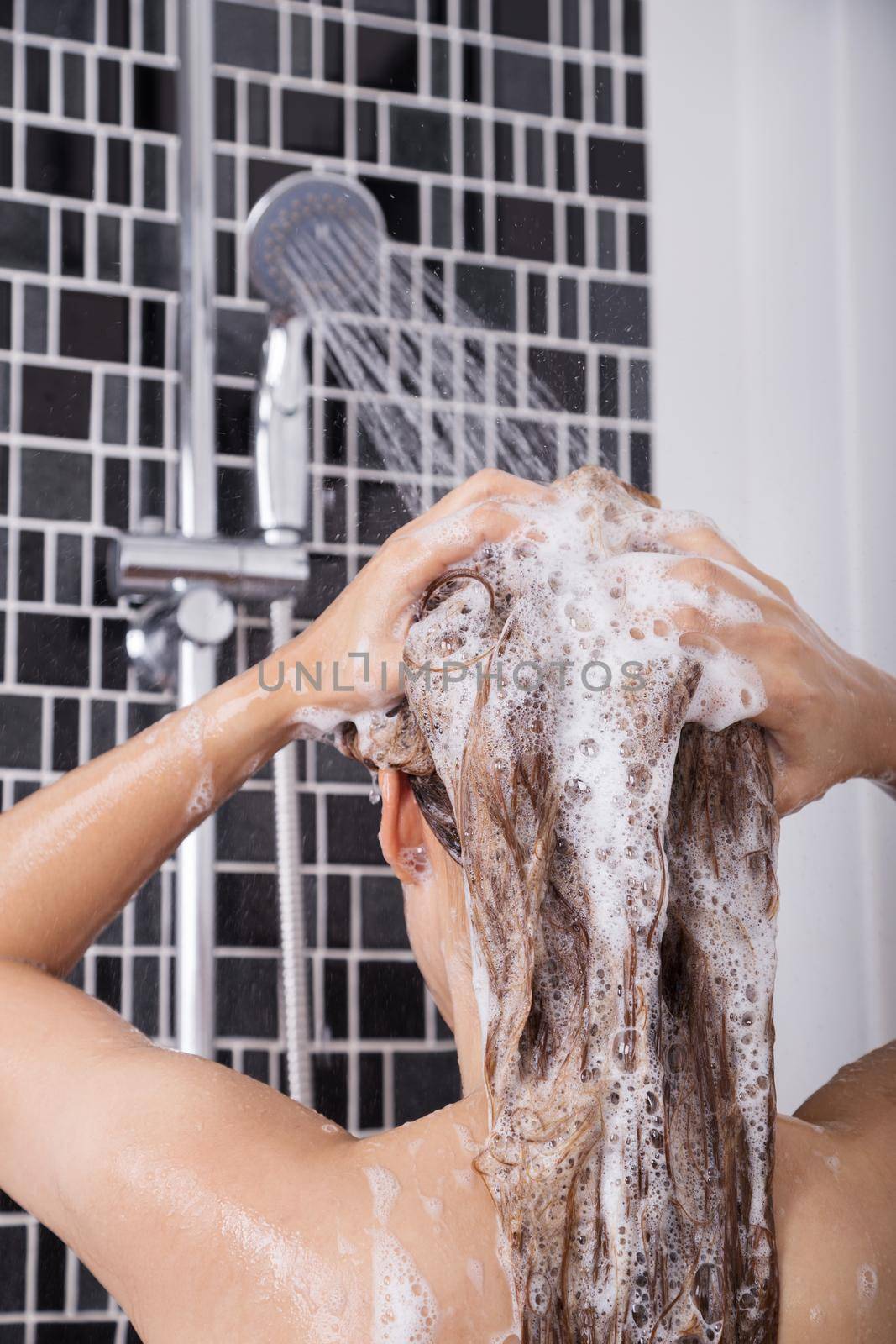 woman washing her head and hair in the shower by shampoo, rear view