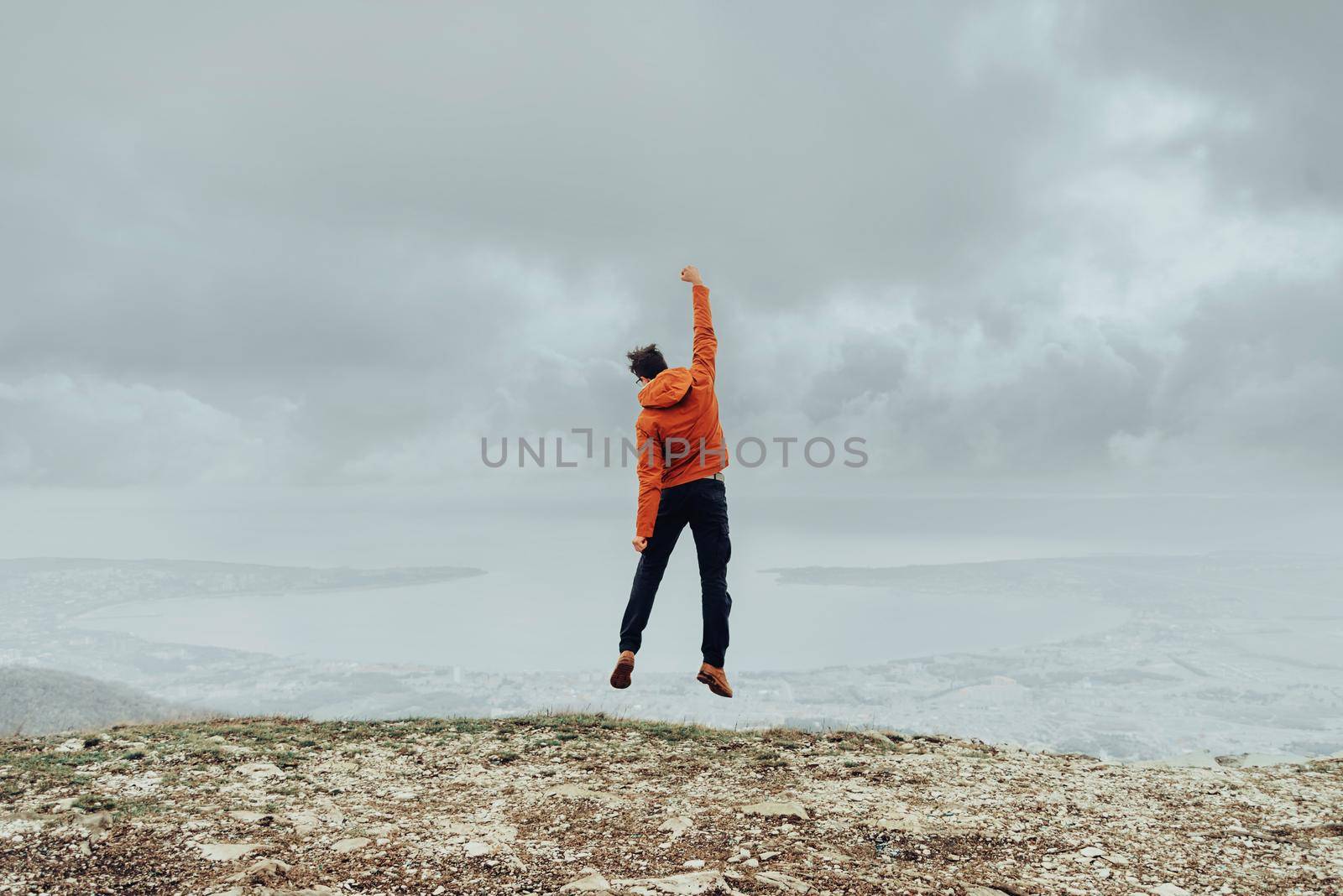 Happy explorer young man jumping on peak of mountain in rainy weather outdoor