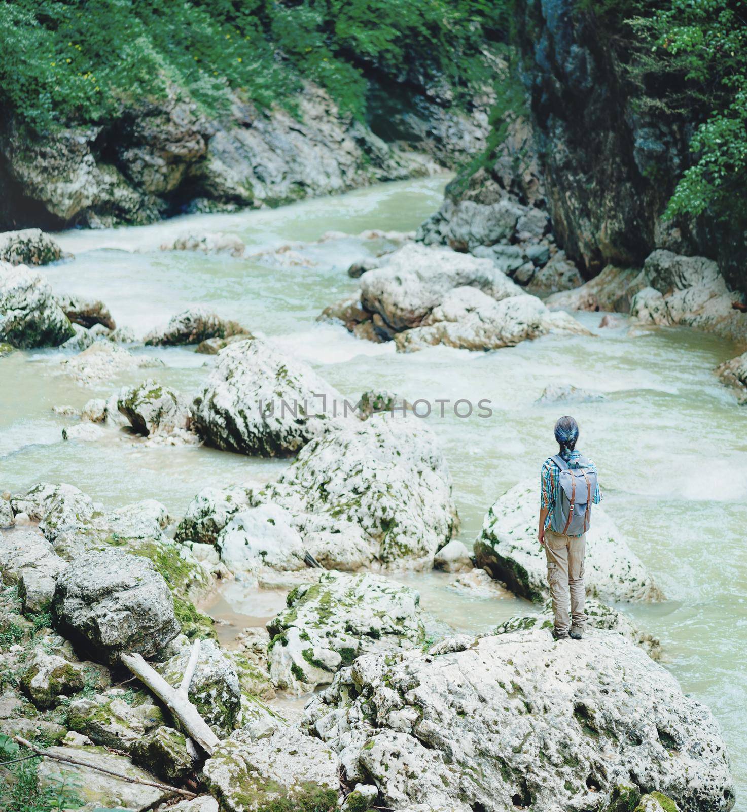 Traveler young woman standing on rocky stone and looking on mountain river in summer