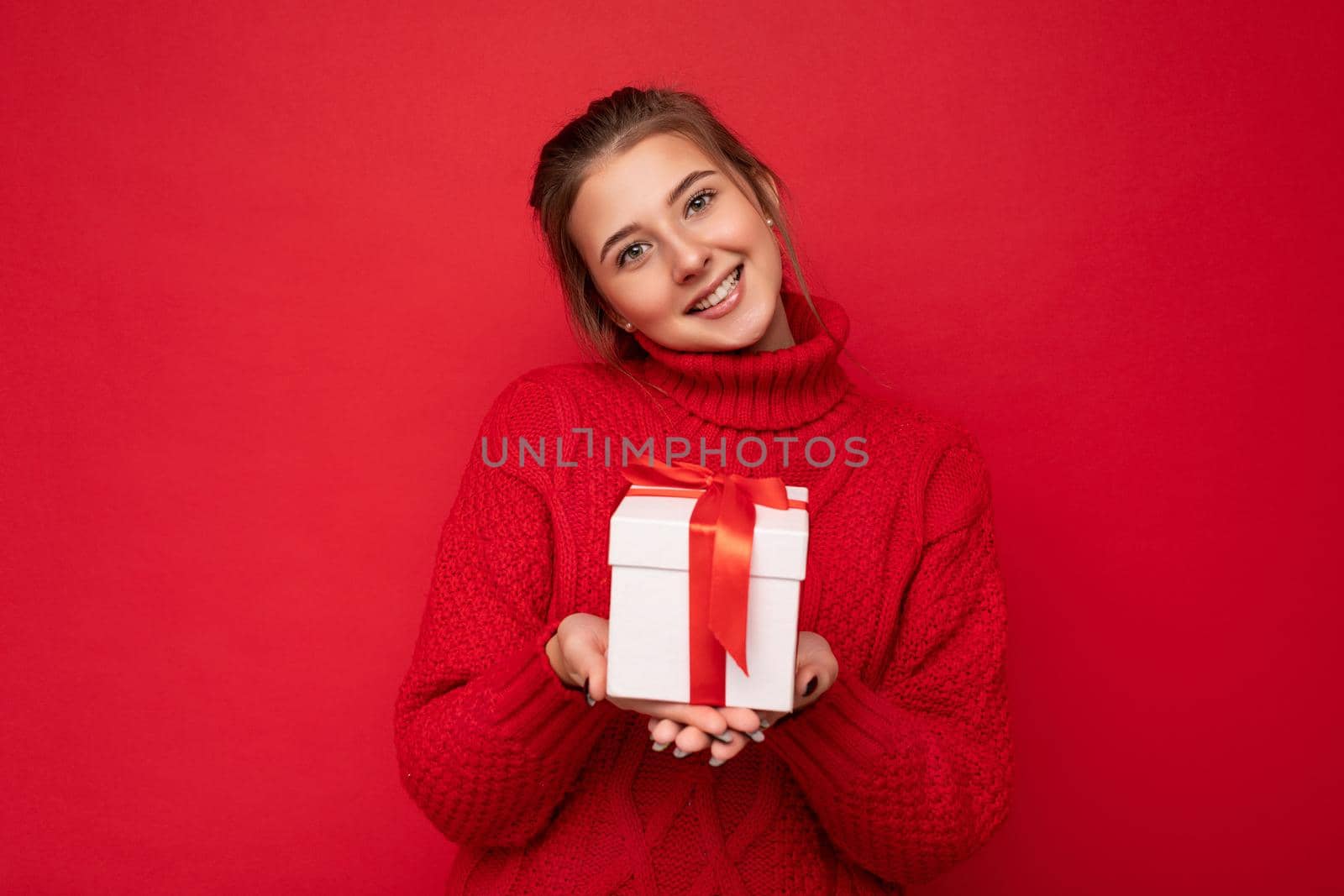 Beautiful happy young brunette woman isolated over colourful background wall wearing stylish casual clothes holding gift box and looking at camera.