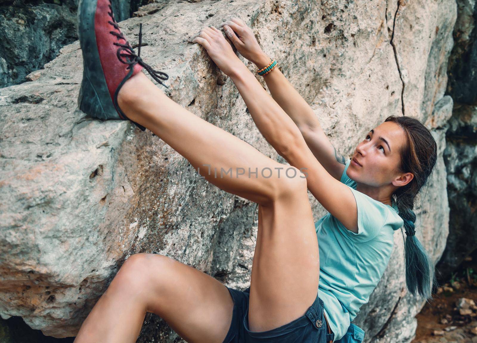 Sporty young woman bouldering the rocky stone outdoor
