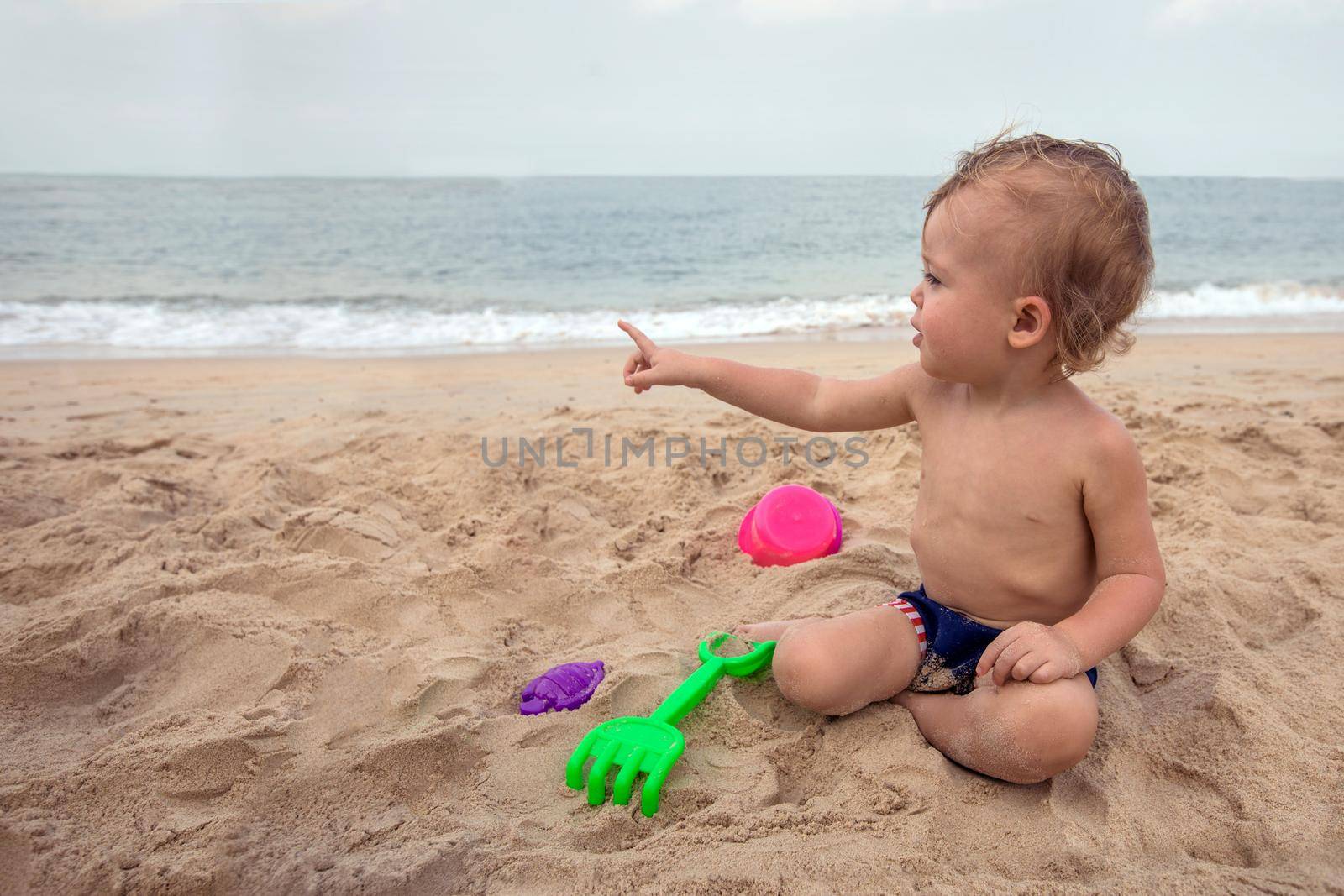 Cute baby boy playing with beach toys. The kid is pointing at something