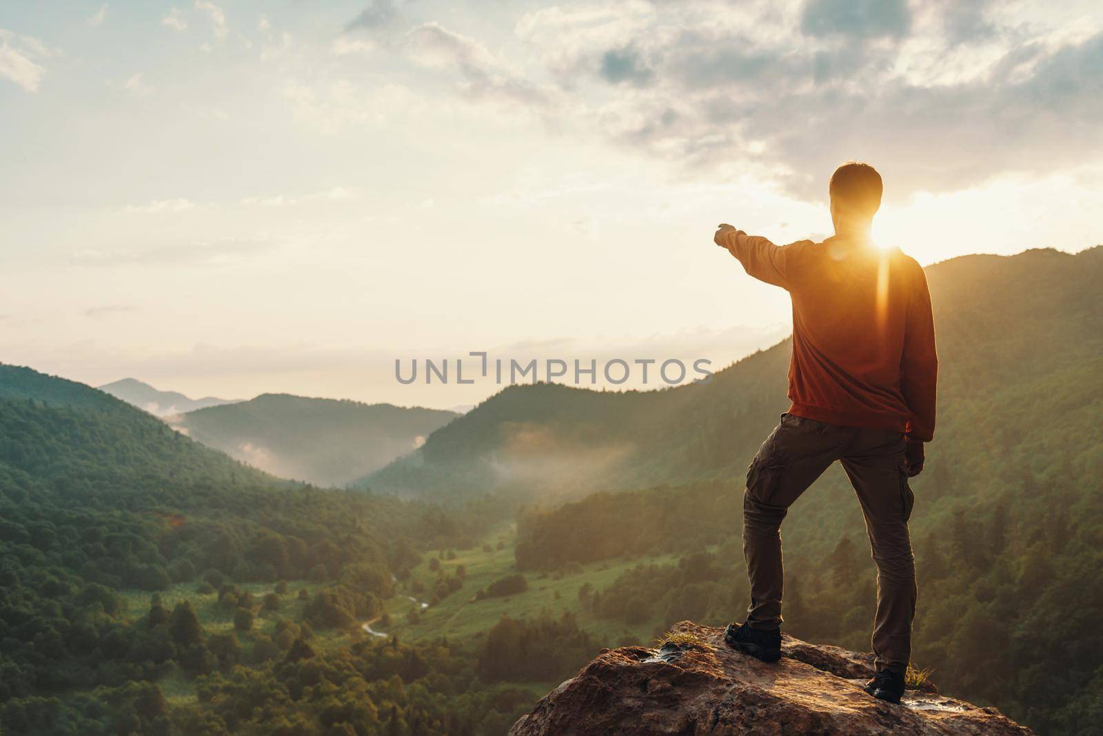 Young man pointing at something in the distance in summer mountains at sunset