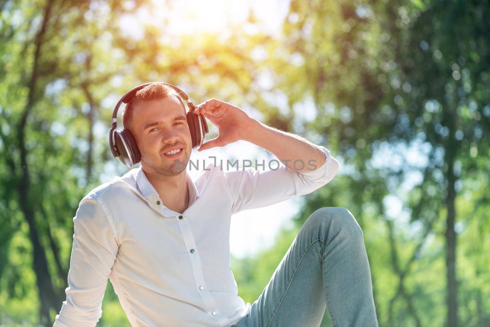 Young man in the park listens to music. He sits on the grass and enjoys music.