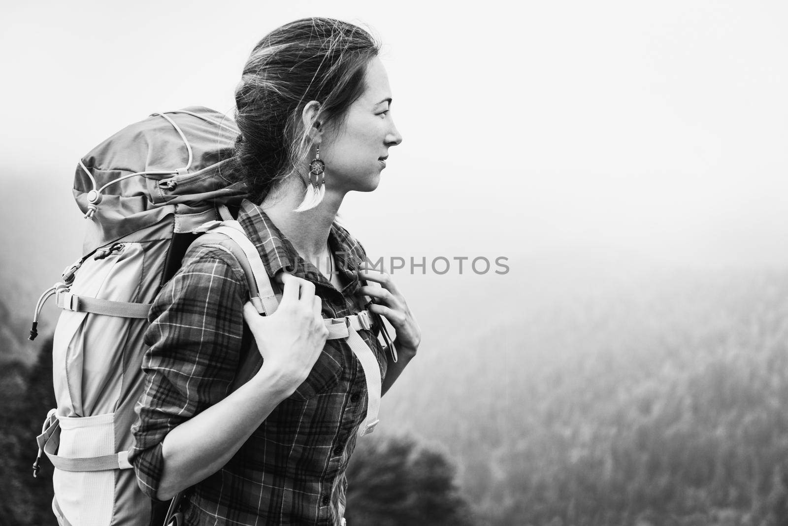 Beautiful hiker young woman with backpack looking at the mountains in summer. Monochrome image.