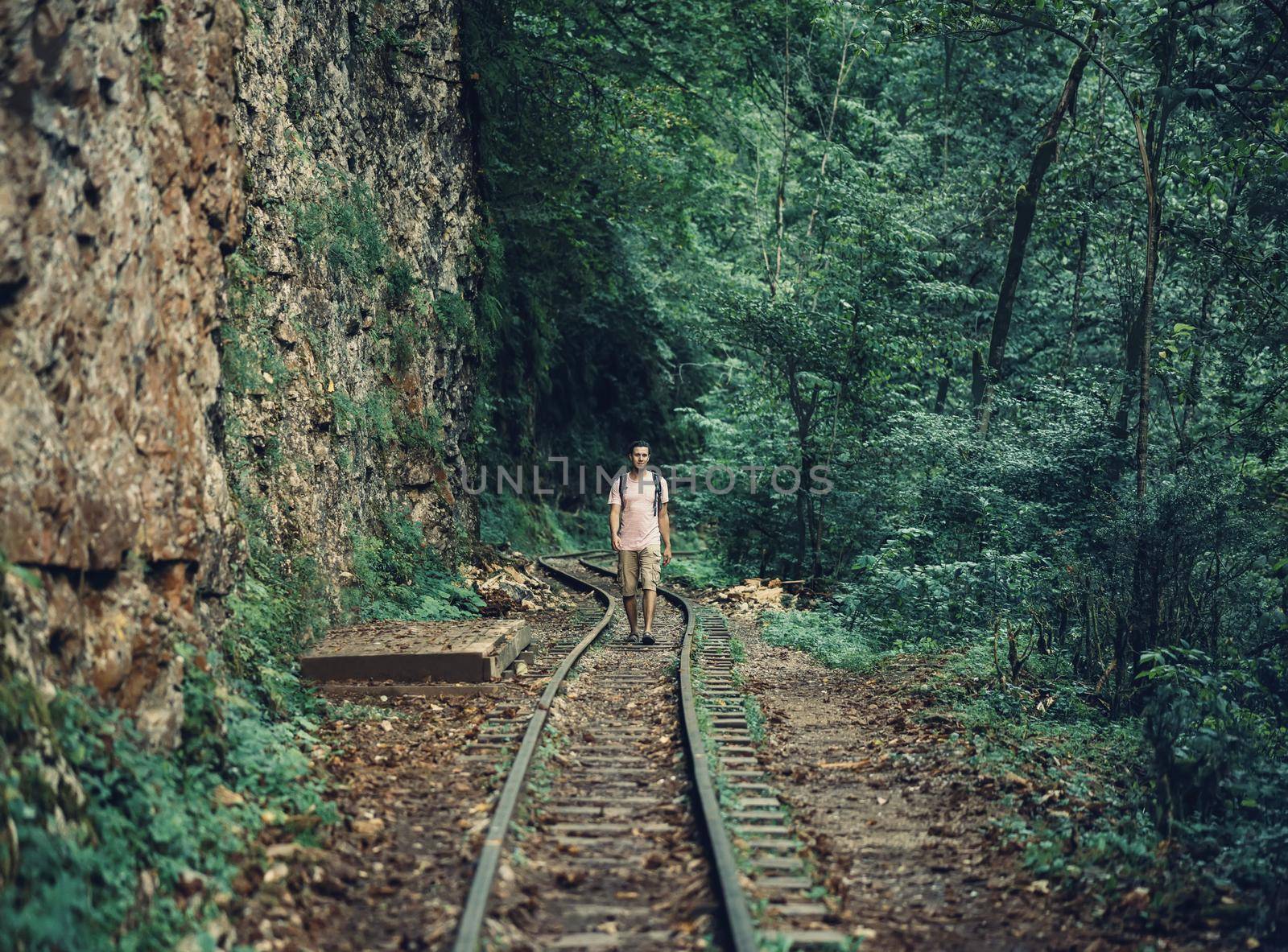 Traveler young man walking on railroad in summer gorge near the cliff