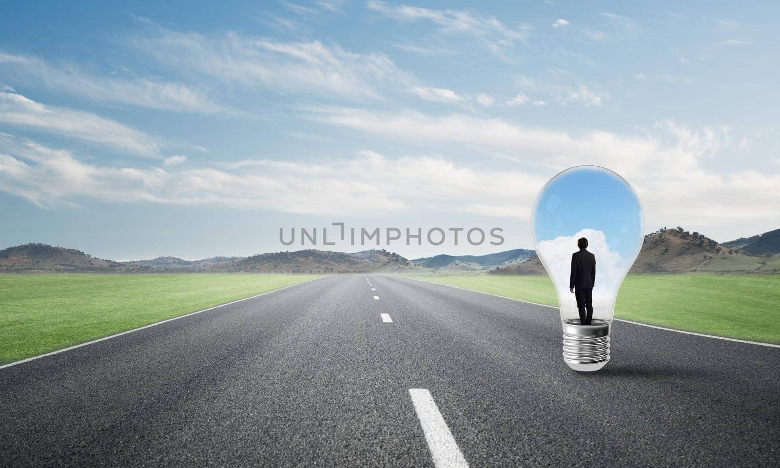 Young businessman trapped inside of light bulb on asphalt road