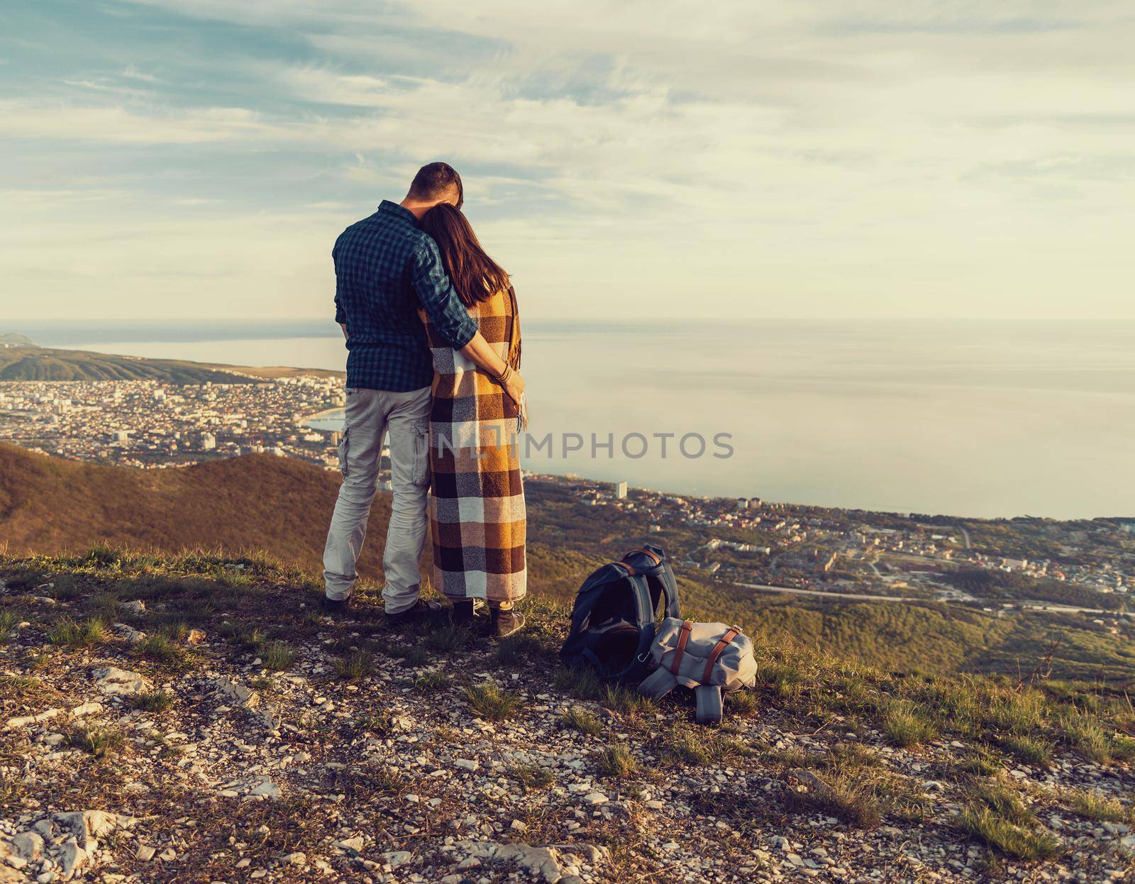 Travelers loving couple standing in the mountains and enjoying view of sea, rear view. Man embracing a woman