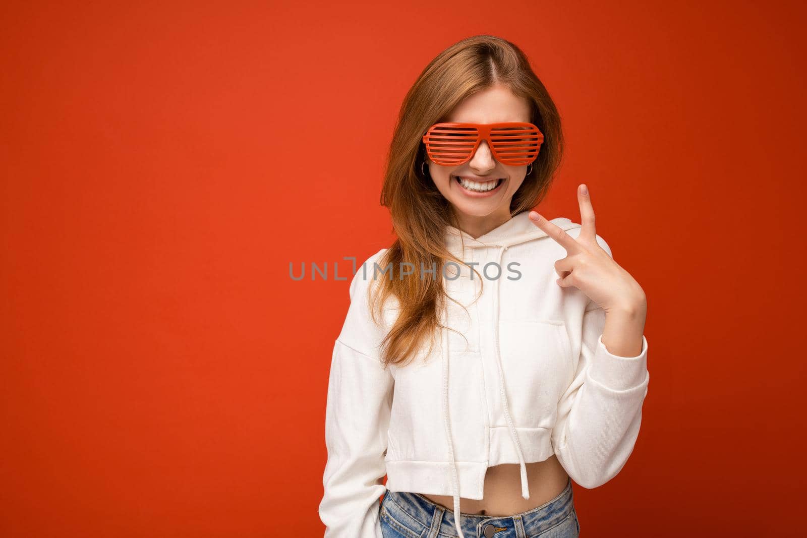 Photo shot of beautiful positive young blonde woman wearing casual clothes and stylish optical glasses isolated over colorful background wall looking at camera.