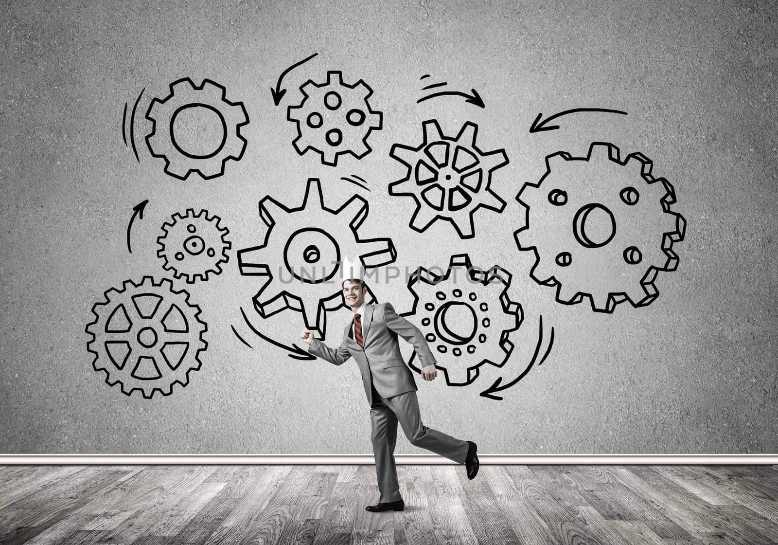 Young handsome businessman wearing white paper crown running and gear mechanism on wall