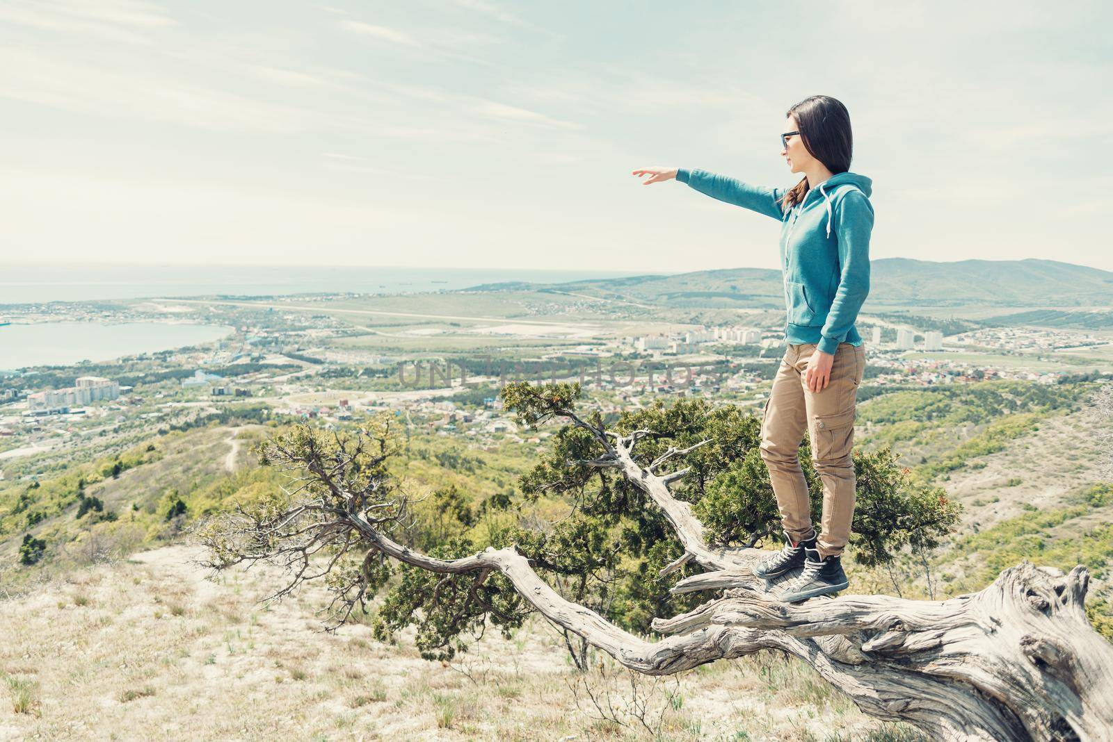 Traveler young woman standing on tree and pointing at something into the distance outdoor