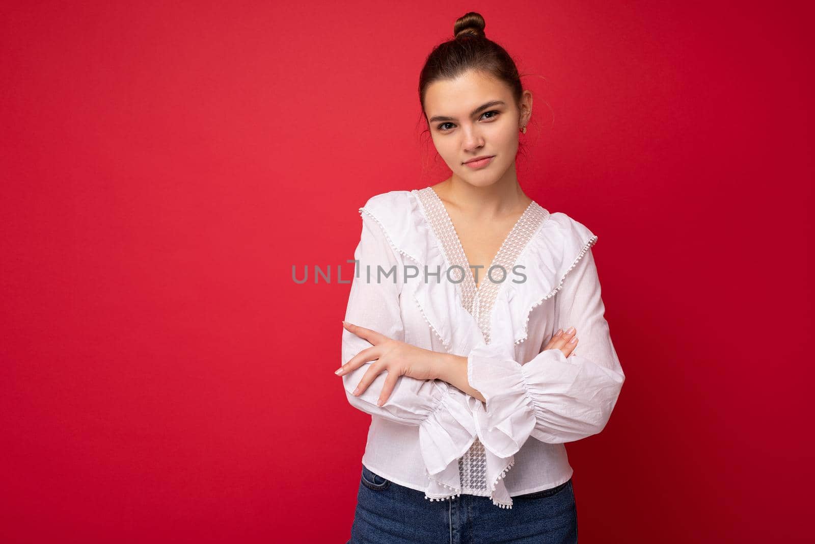 Portrait of young attractive caucasian hipster woman in trendy casual clothes. Sexy carefree female person posing isolated near red wall in studio. Positive model with natural makeup. Empty space.