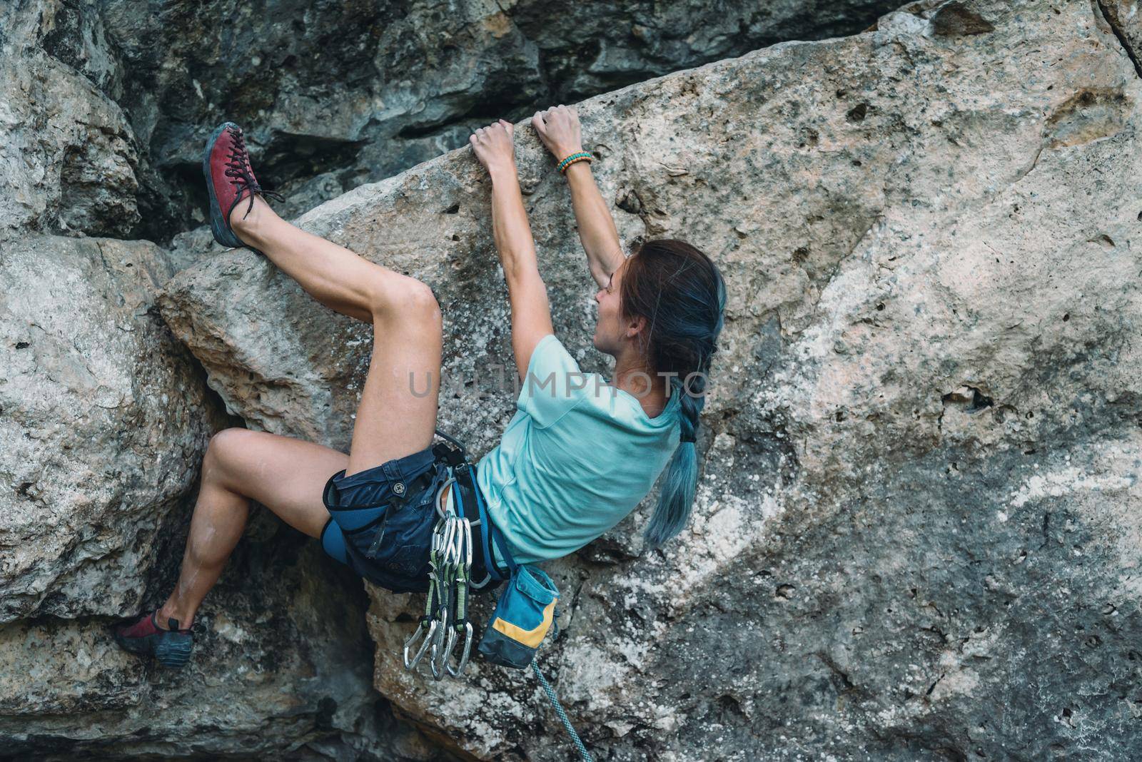 Sporty young woman in safety harness with outfit started to climbing the rock wall outdoor