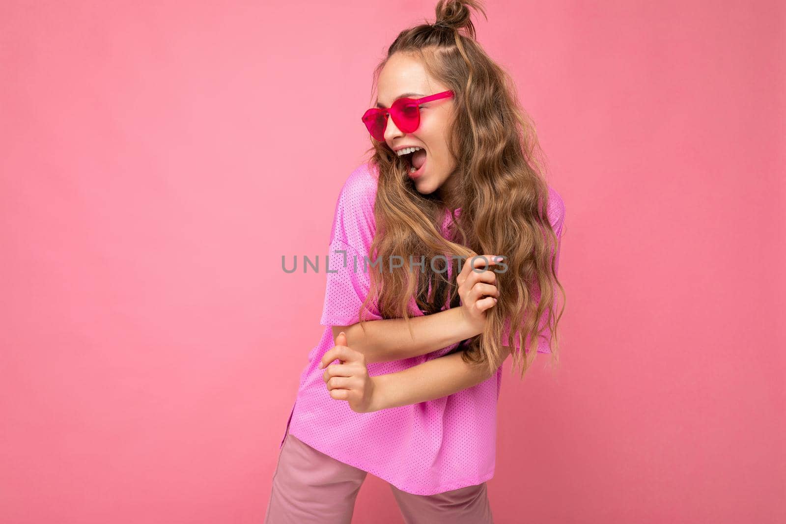 Attractive funny positive joyful young blonde woman wearing everyday stylish clothes and modern sunglasses isolated on colorful background wall looking to the side.
