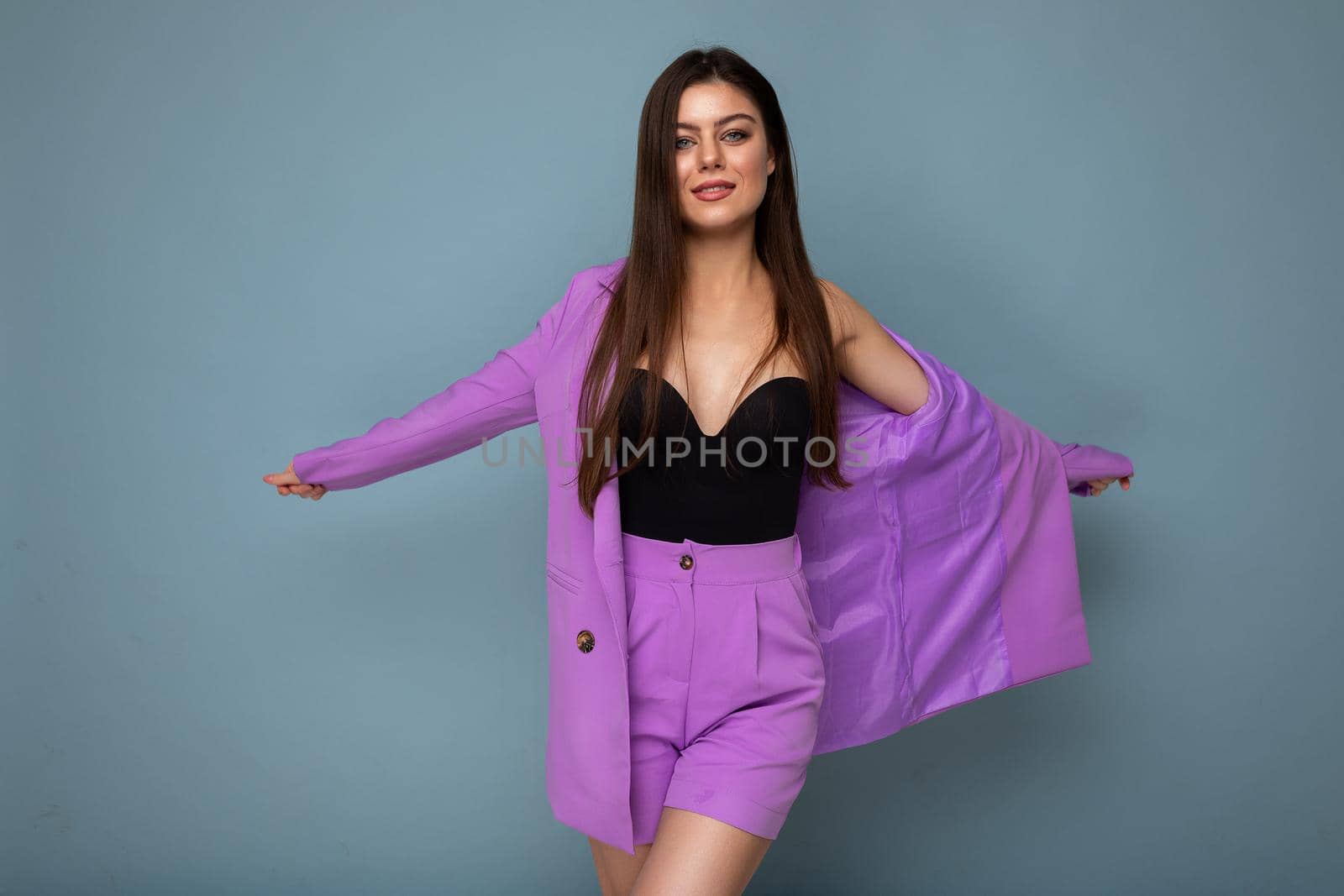 Portrait of happy positive beautiful fashionable brunette woman in casual trendy violet jacket isolated on blue background with free space.