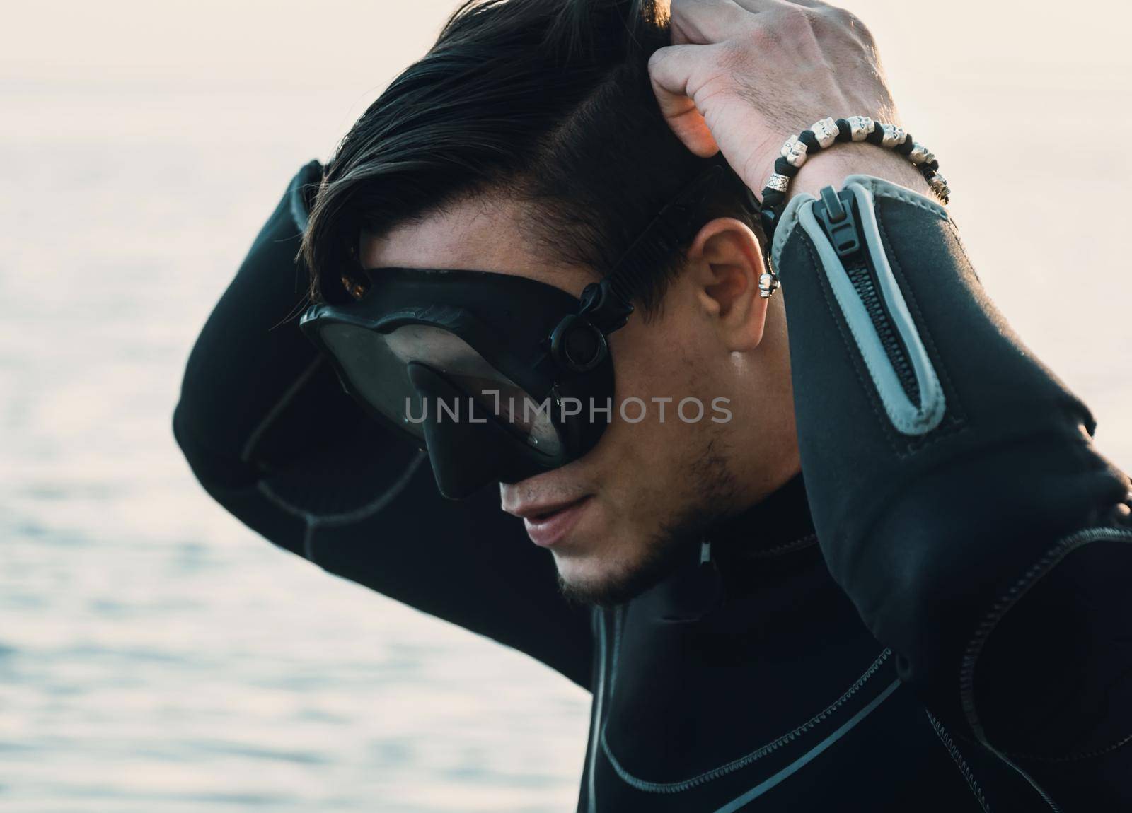 Diver young man puts on a mask on background of sea, close-up