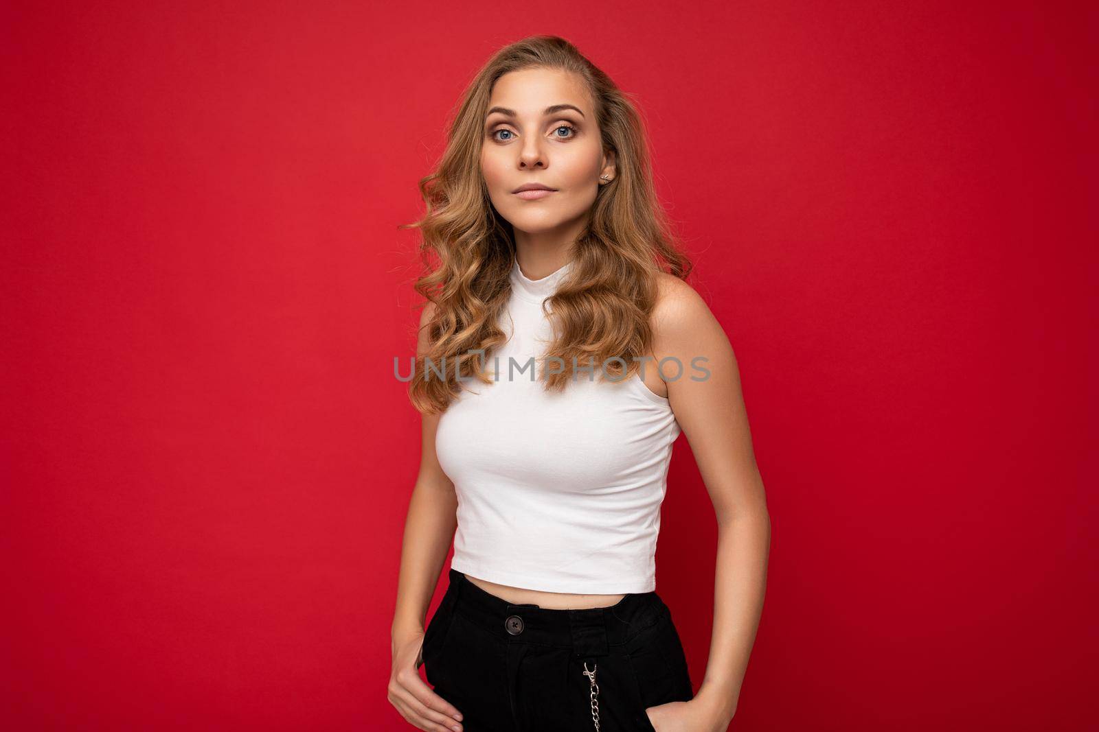 Portrait photo of young beautiful pretty self-confident assertive cool blonde woman with sincere emotions wearing stylish white top isolated over red background with free space.