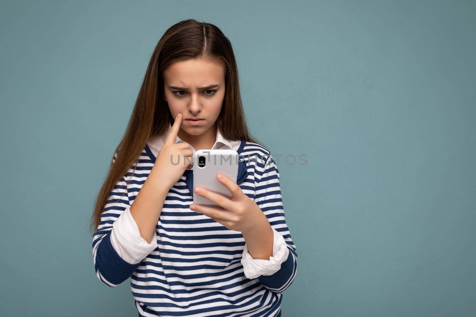 Beautiful young girl wearing casual clothes standing isolated over background surfing on the internet via phone looking at mobile screen.