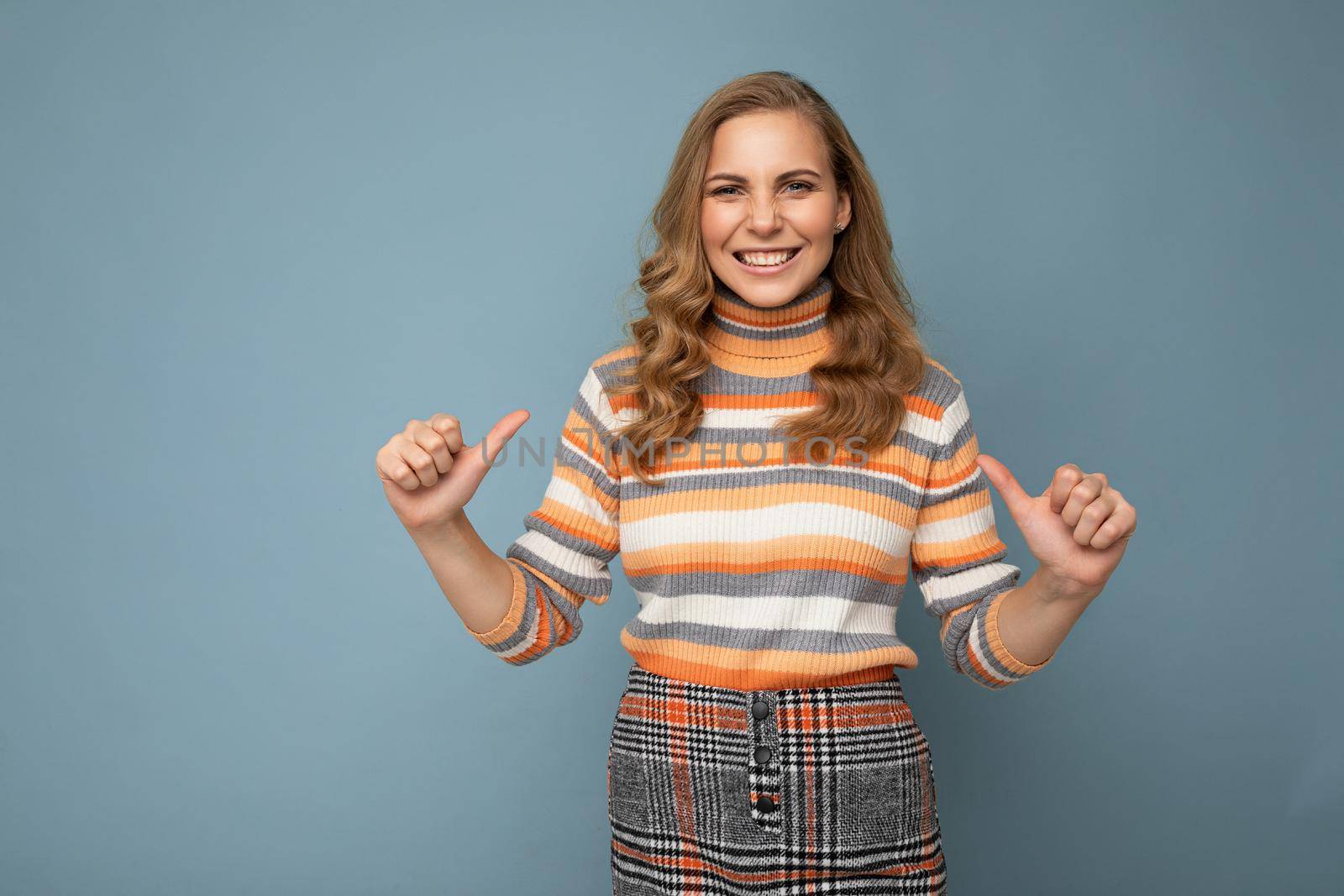 Young charming fascinating sexy positive happy smiling blonde woman wearing casual striped pullover isolated over blue background with free space and points fingers at herself.