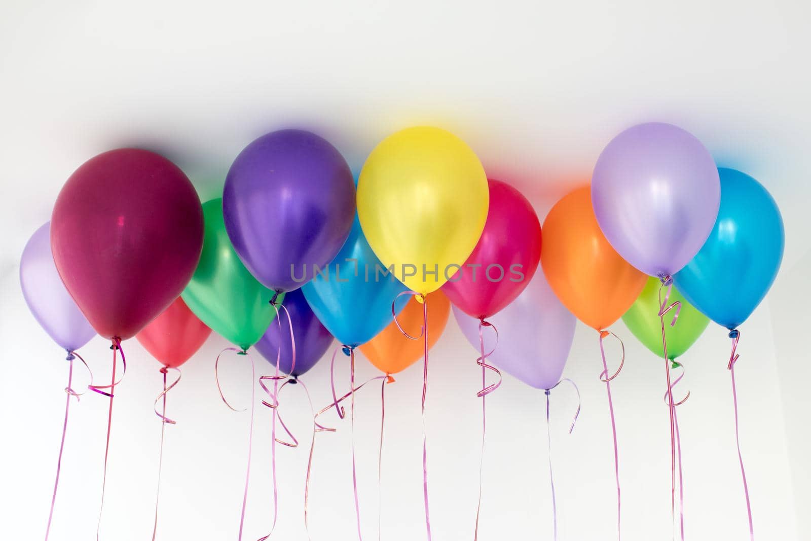 Bright different colored helium balloons hanging under white ceiling.