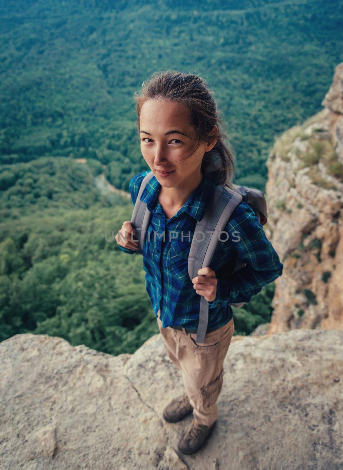 Smiling traveler young woman with backpack in summer mountains, funny view from top