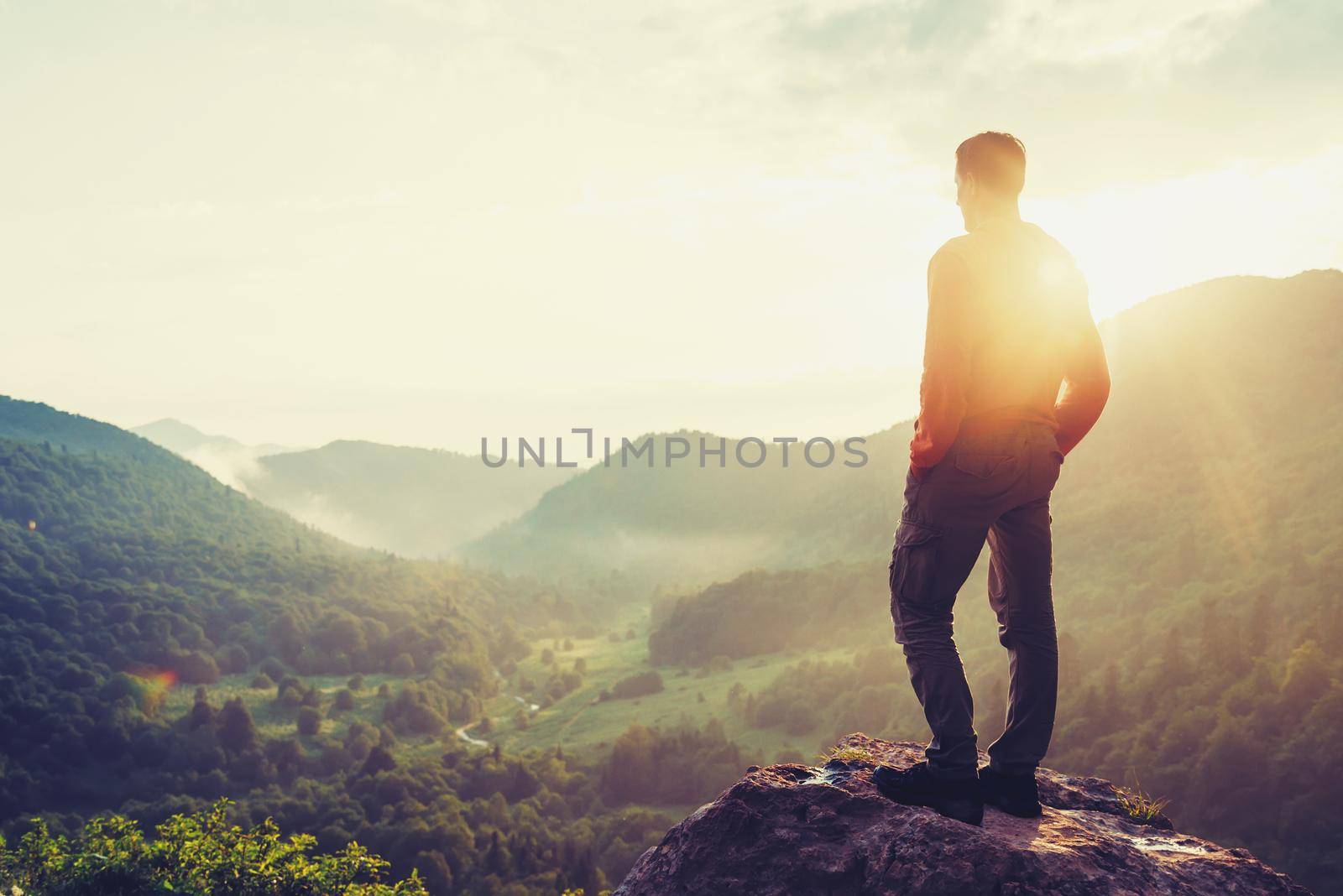 Traveler young man standing in the summer mountains at sunset and enjoying view of nature. Image with instagram color by alexAleksei