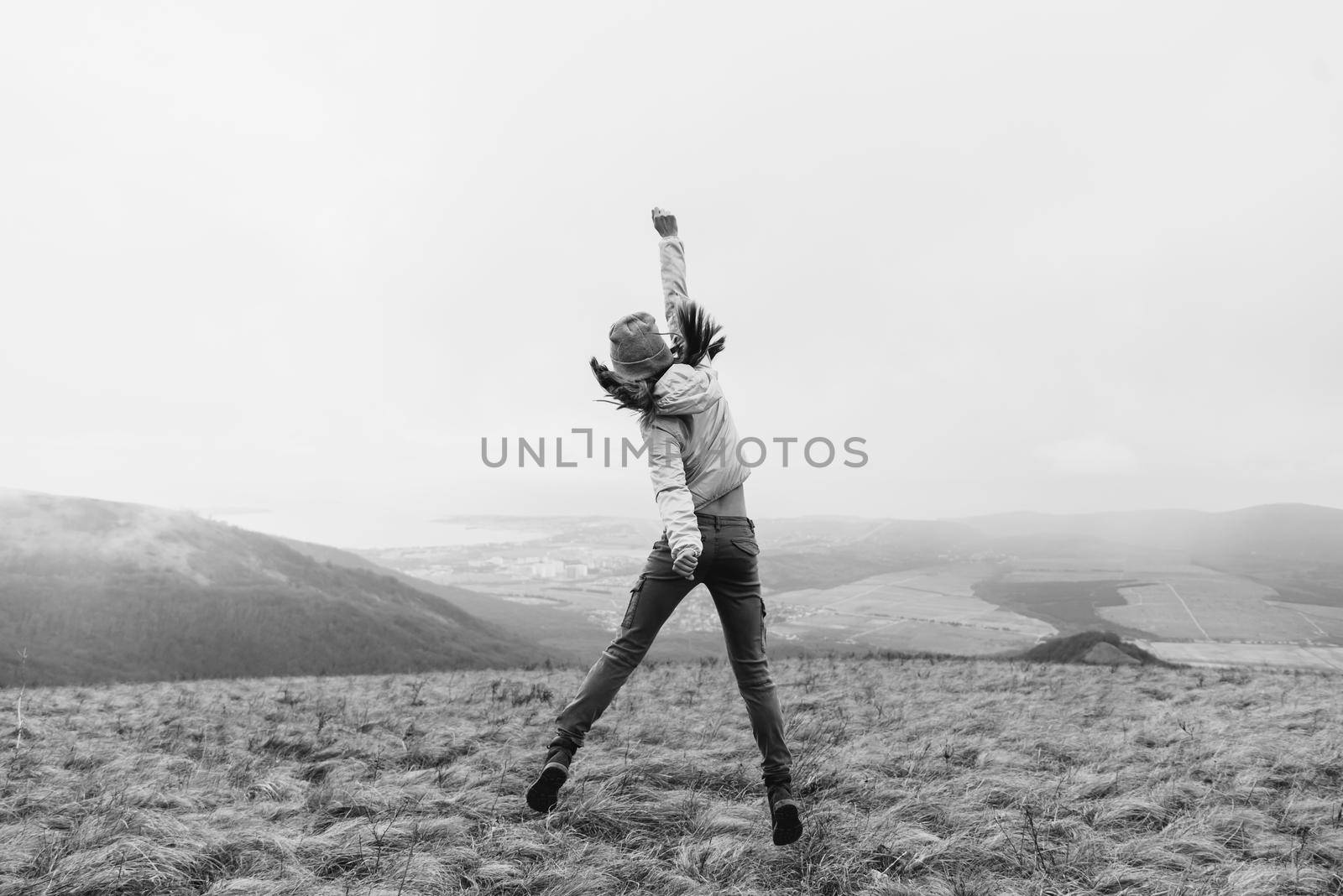 Unrecognizable happy young woman jumping on meadow in the mountains, rear view. Monochrome image