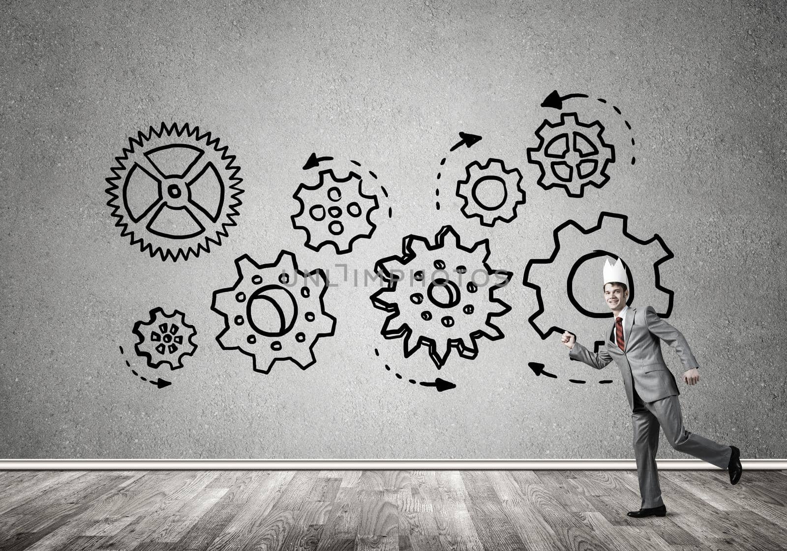 Young handsome businessman wearing white paper crown running and gear mechanism on wall