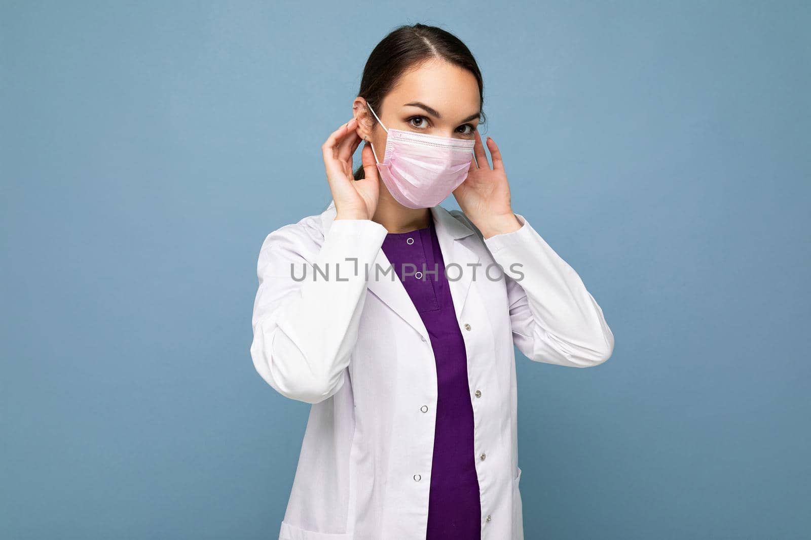 Beautiful young woman holds and wears a white medical mask to protect yourself from corona virus, cares for her health and safety, sticks to self-isolation. Concept of Covid-19.