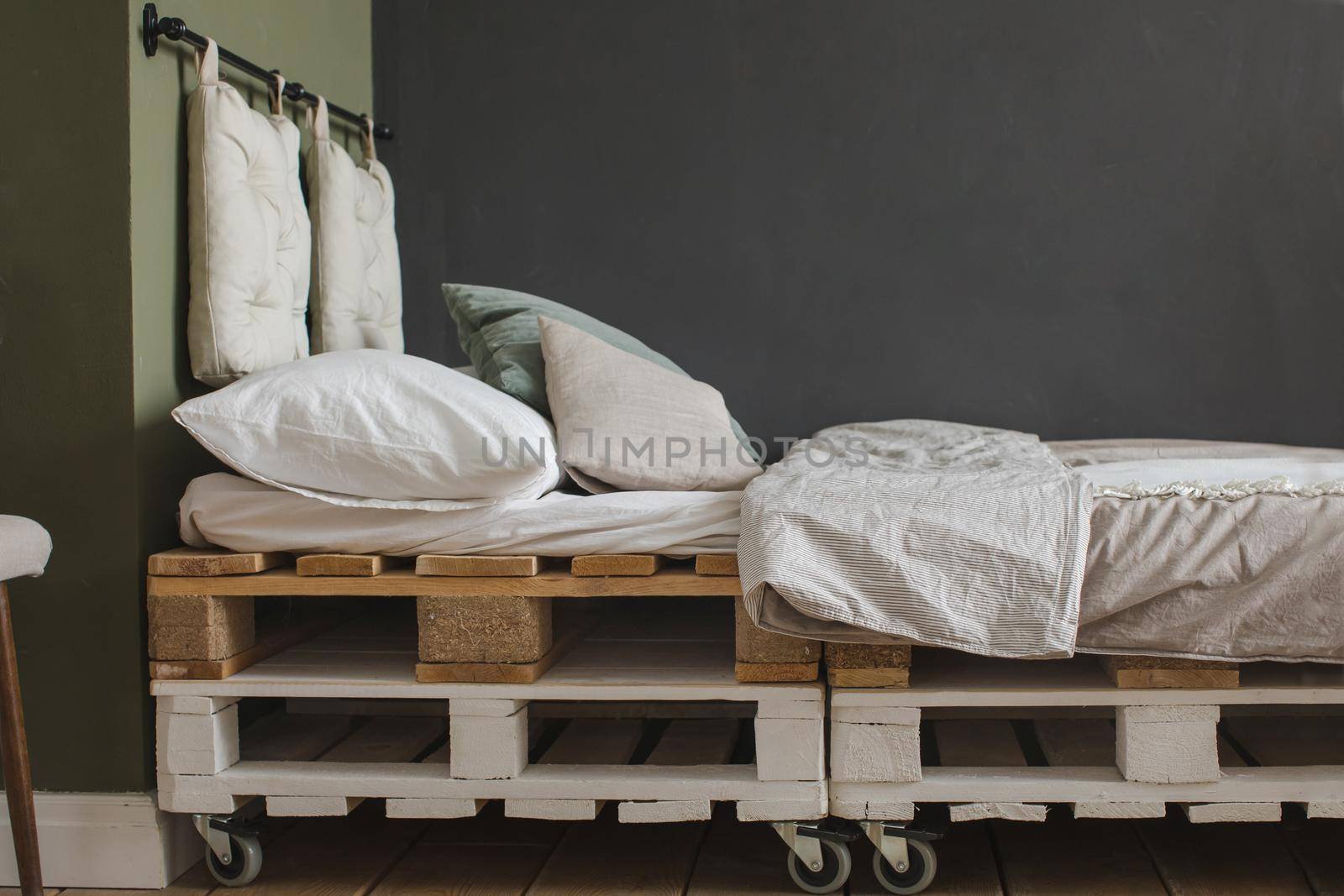 Side view of wooden palettes composed into bed with mattress and cozy pillows.