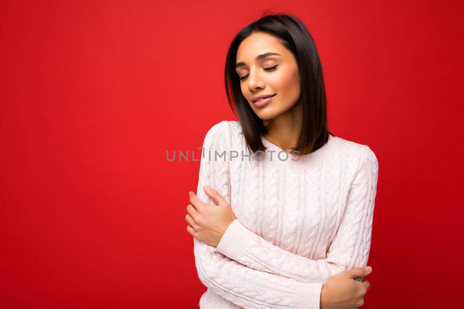 Attractive happy positive cute nice adorable tender young brunette woman in casual light knitted sweater isolated on red background with free space and enjoying.